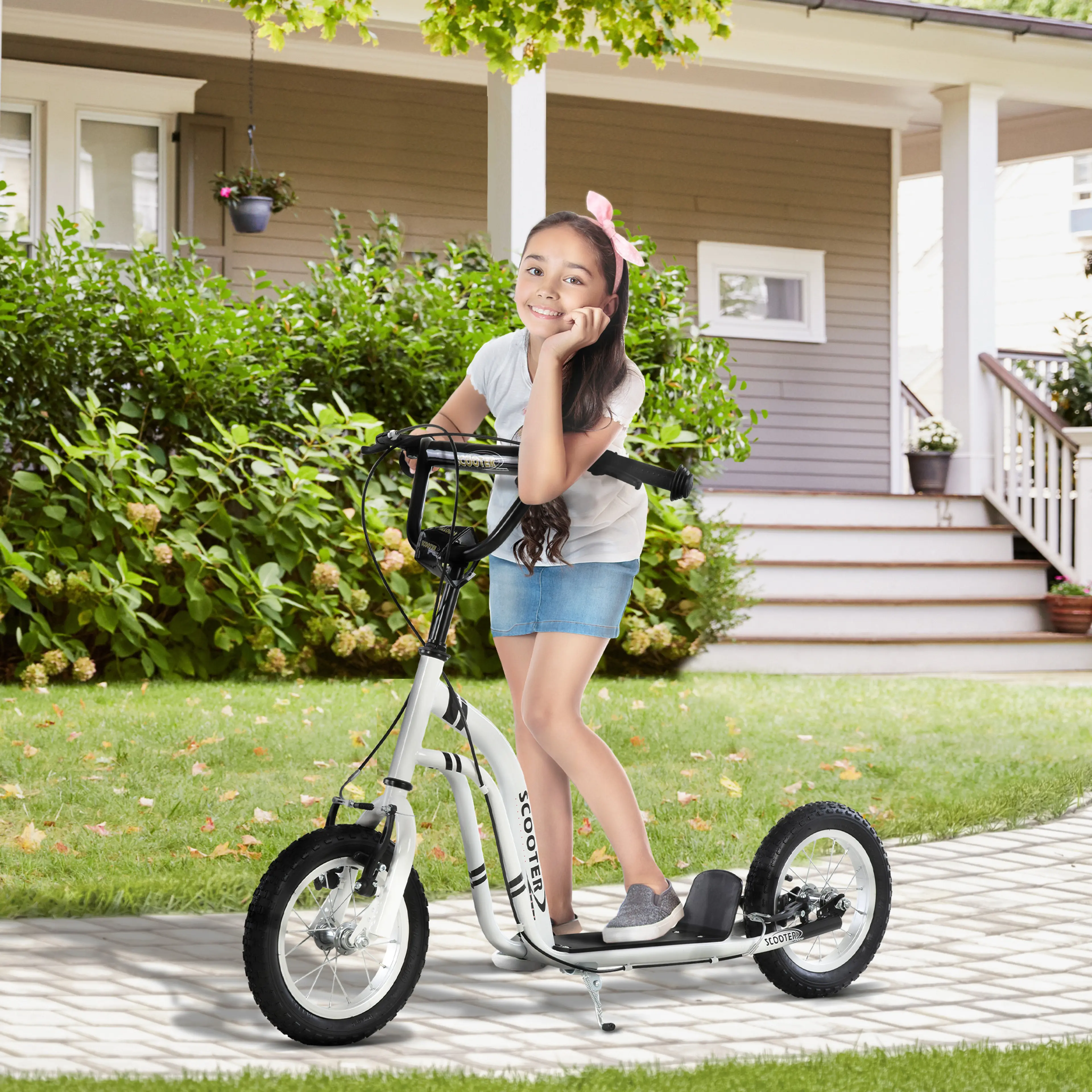 Flicka står på den vita sparkcykeln framför ett hus med trappa