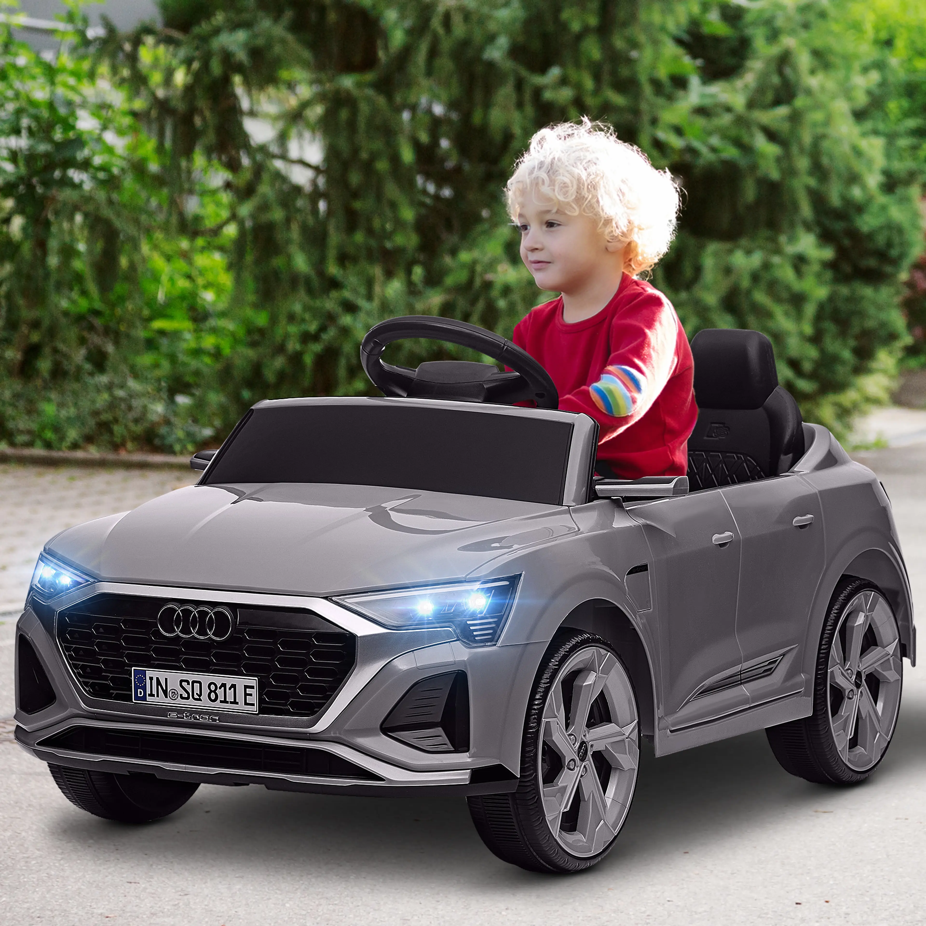Grå elbil barn Audi Q8 e-tron Sportback med ett litet barn bakom ratten på en uppfart