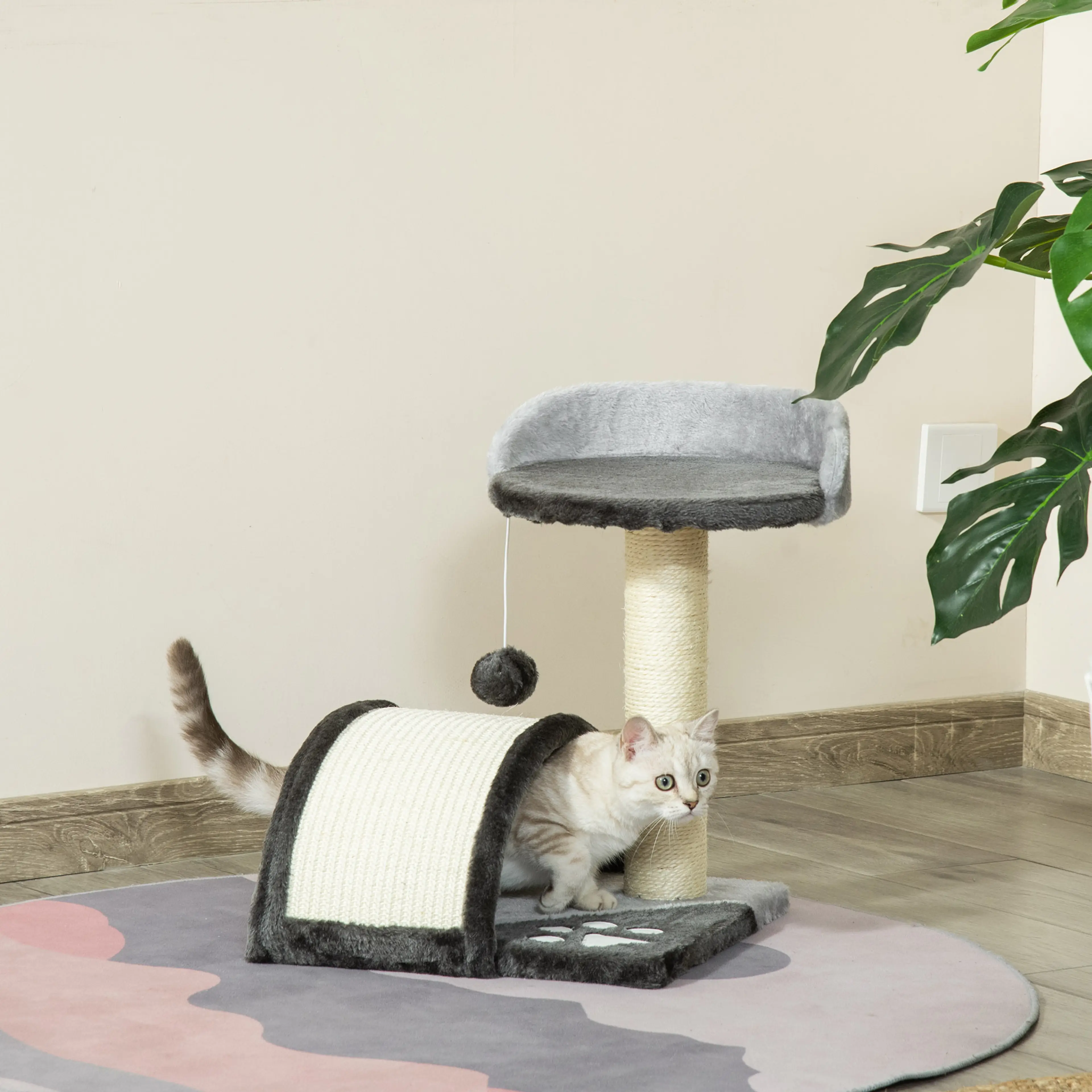 Mörkgrått klösträd på golvet i ett vardagsrum med en katt som kliver ut ur krypinet under klösbrädan