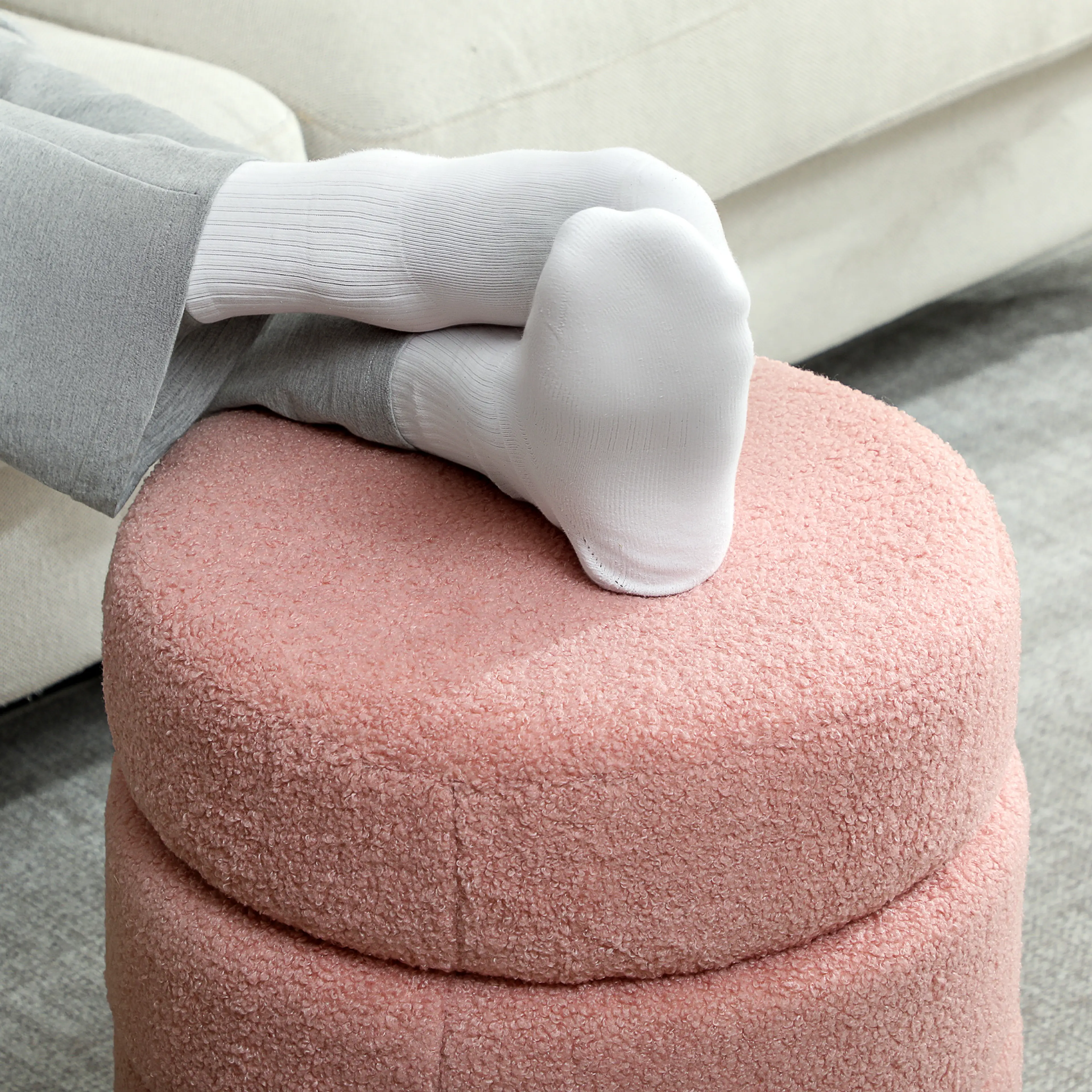 Fötter i vita strumpor vilar på den rosa pallen framför en soffa