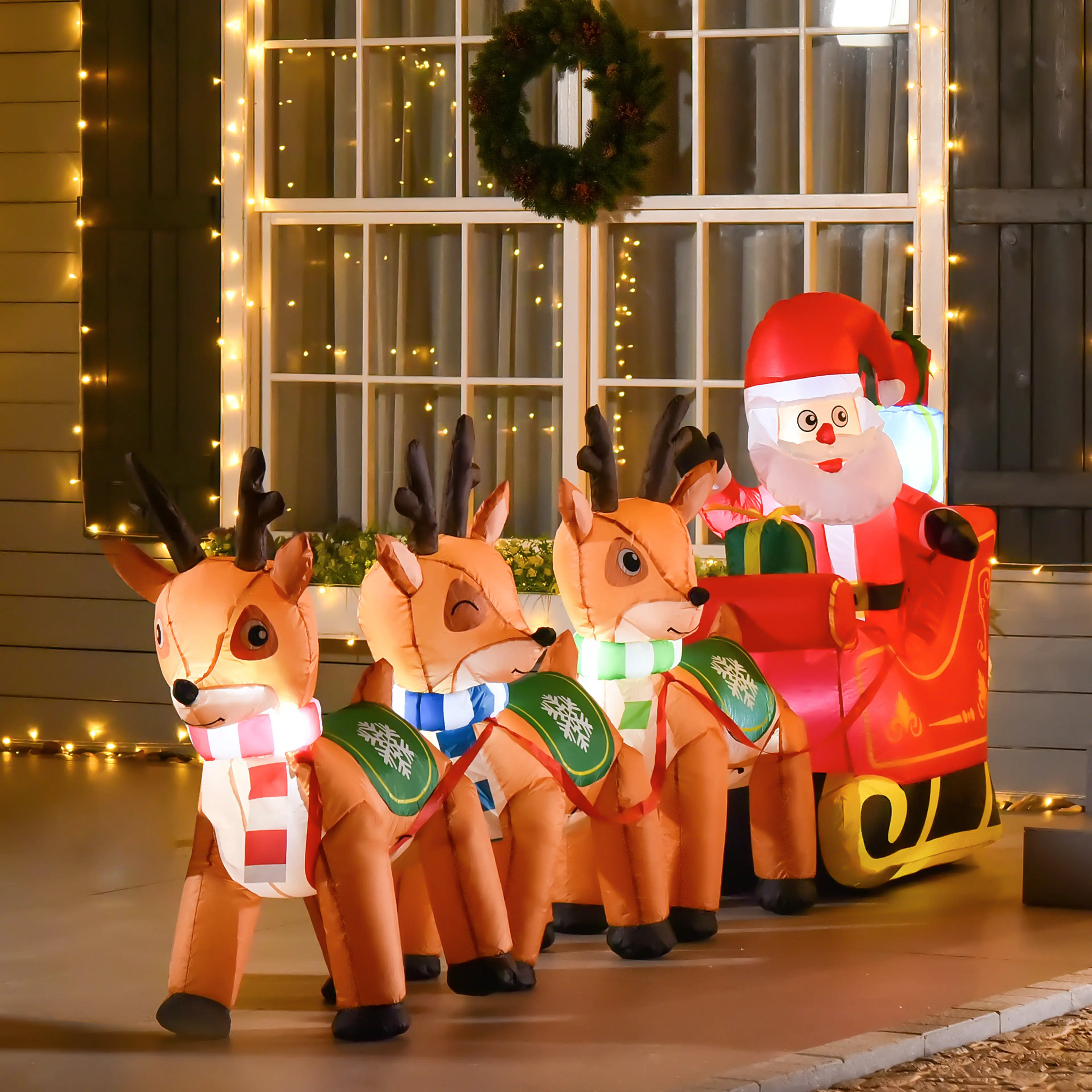 Den upplysta tomten med släde och renar framför ett fönster med julbelysning