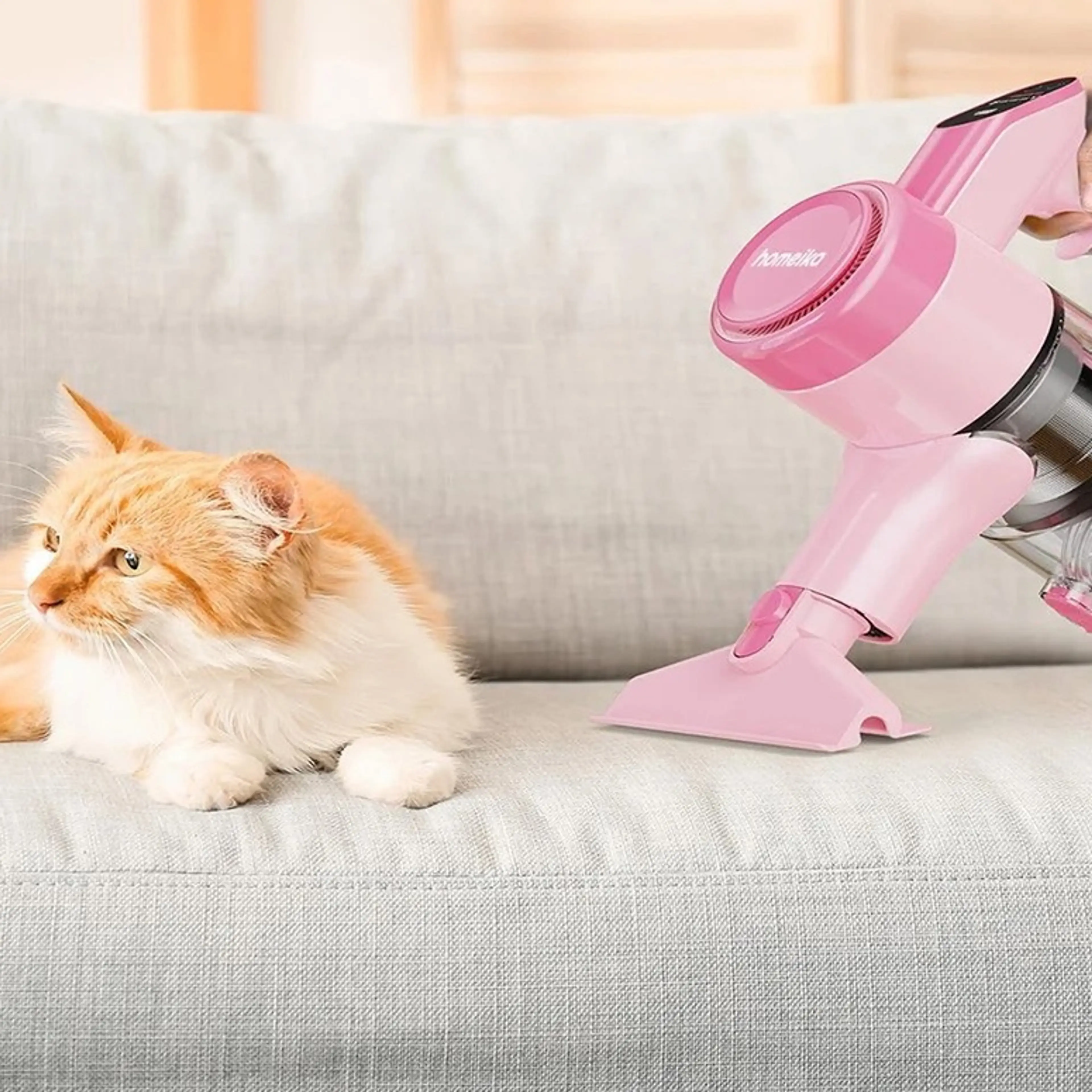 Person dammsuger soffan med den rosa handdammsugaren medan en katt vilar bredvid