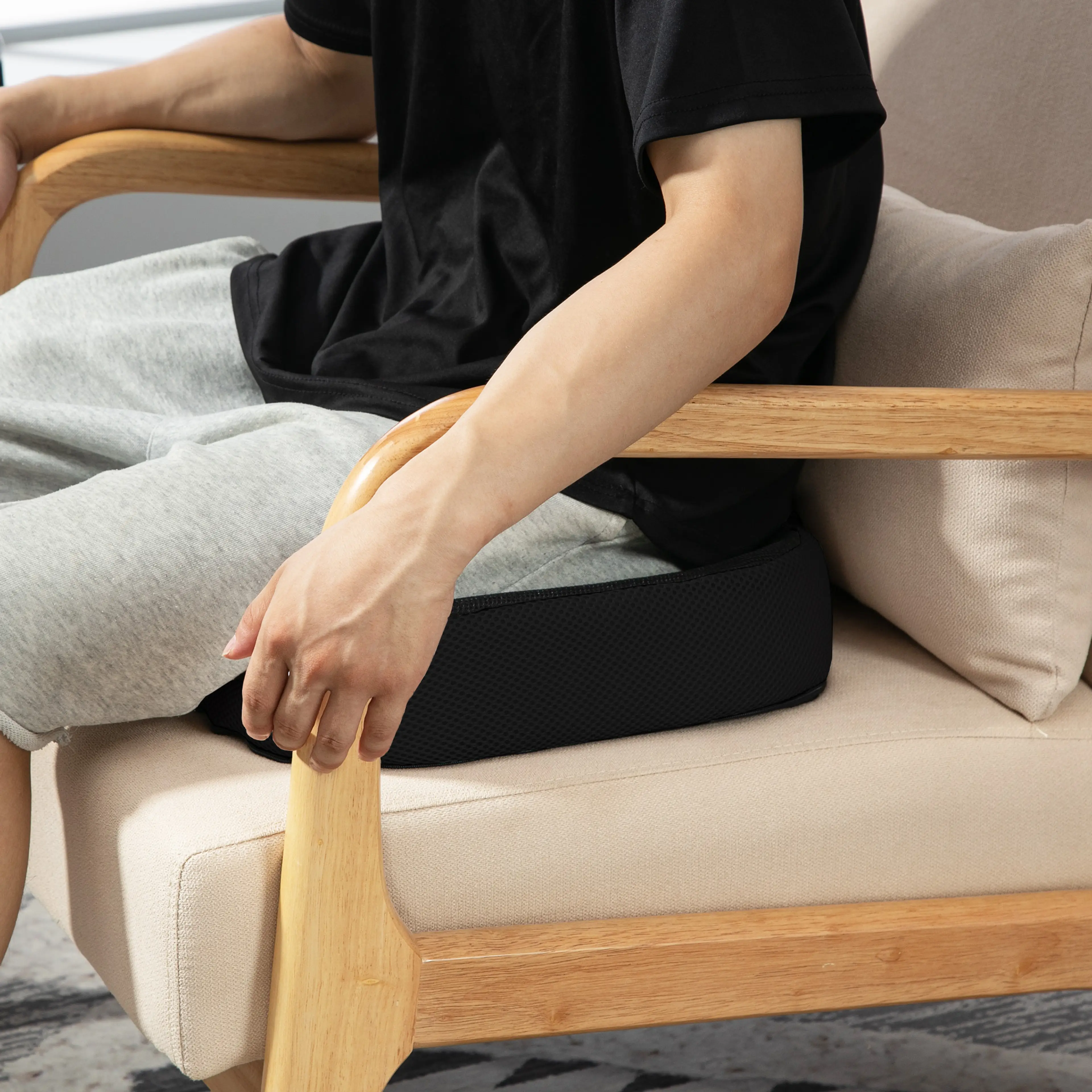 En person sitter på sittdynan i en fåtölj med armstöd i trä