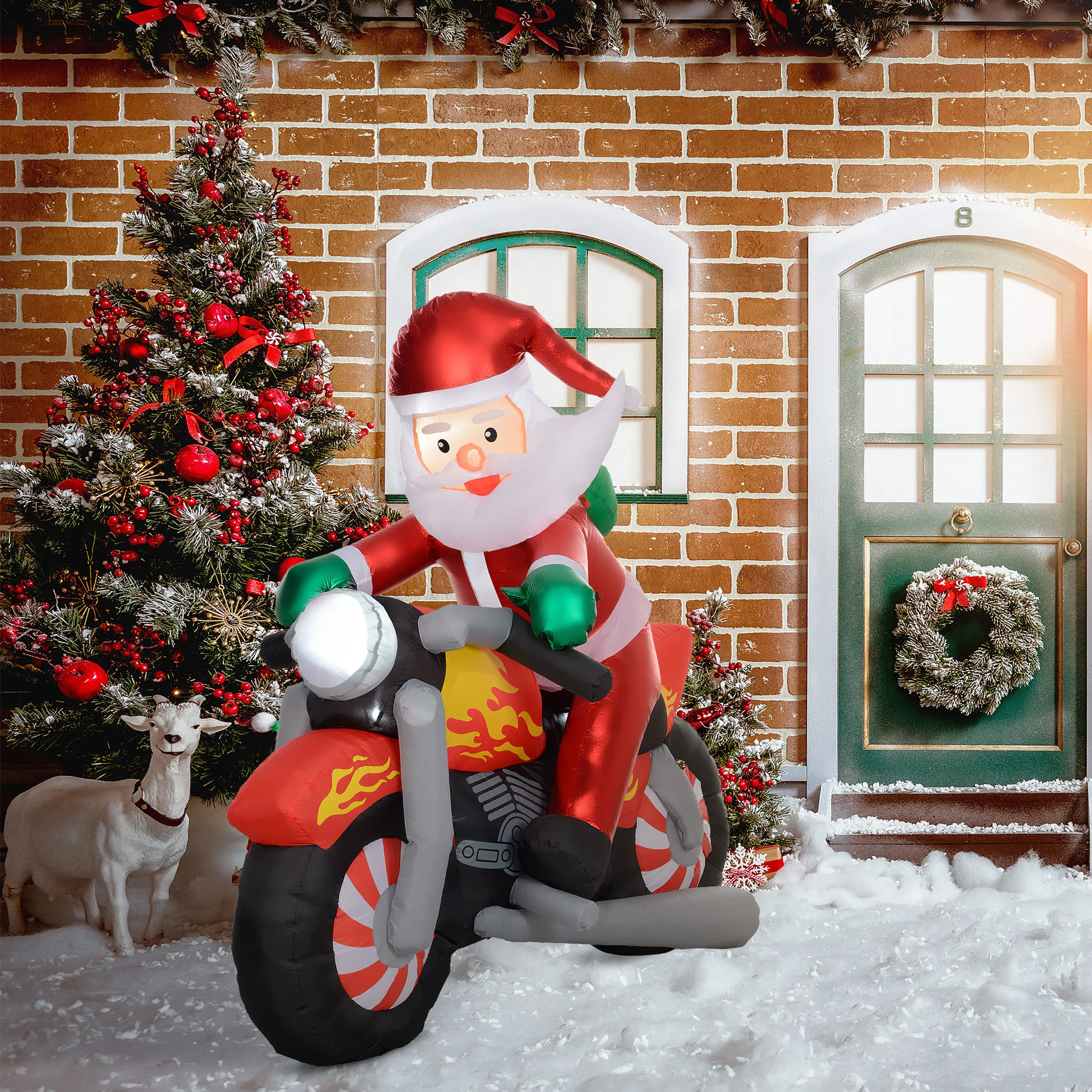 Den uppblåsbara tomten på motorcykeln framför ett tegelhus med en julgran och snö på marken