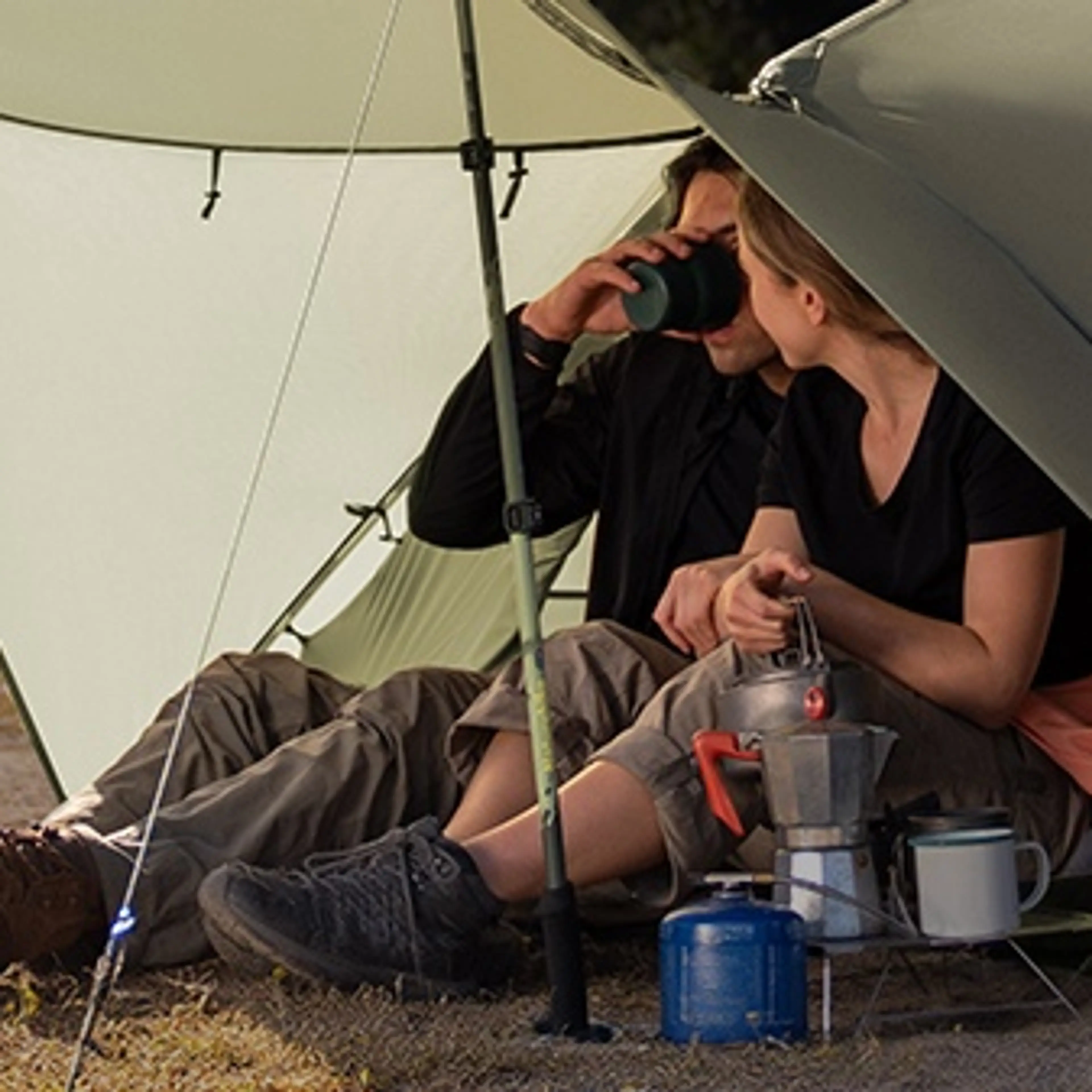 Två personer sitter och lagar kaffe under Mongar Pros utspända soltak i skymningen