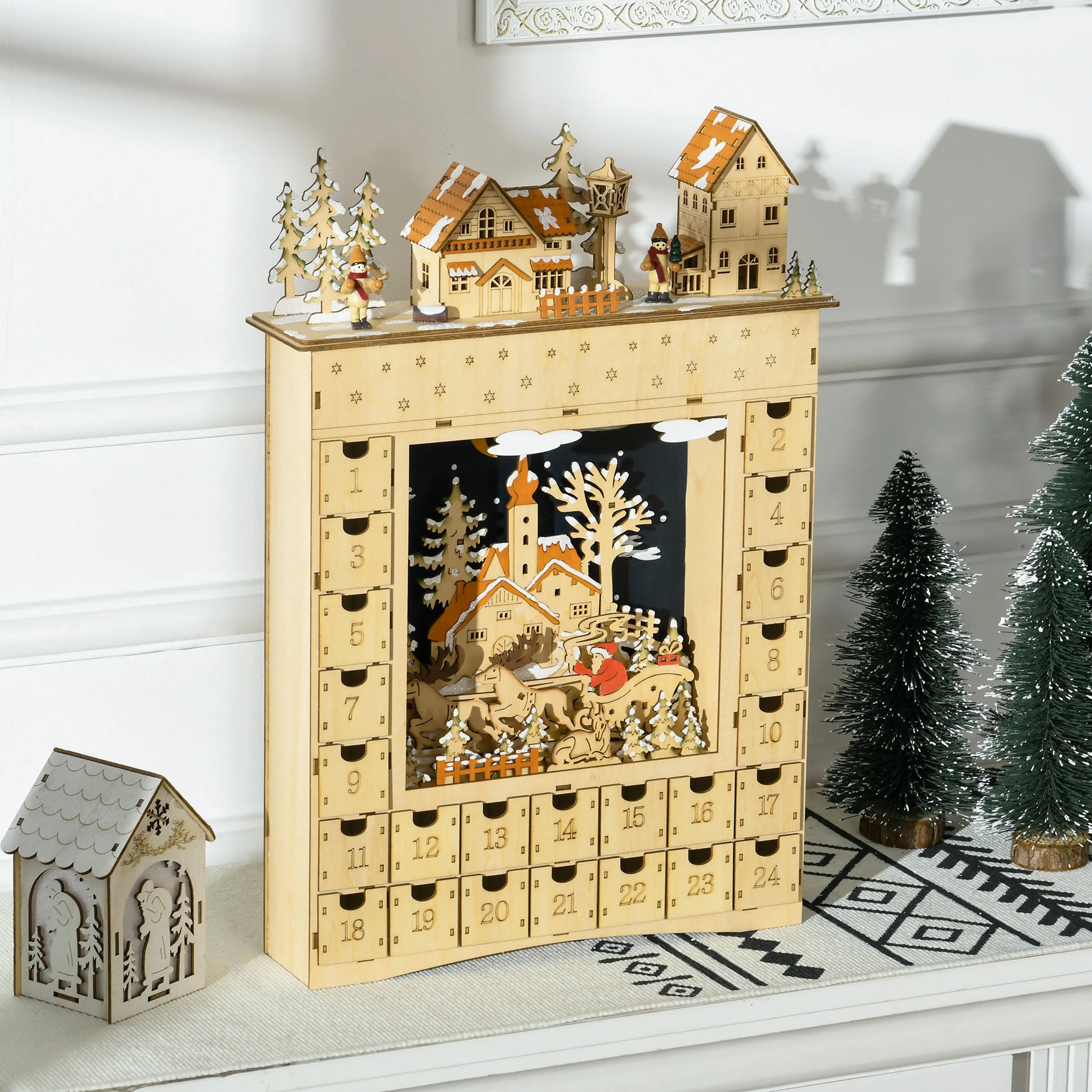 Adventskalendern på en bänk bredvid små granar och ett trähus