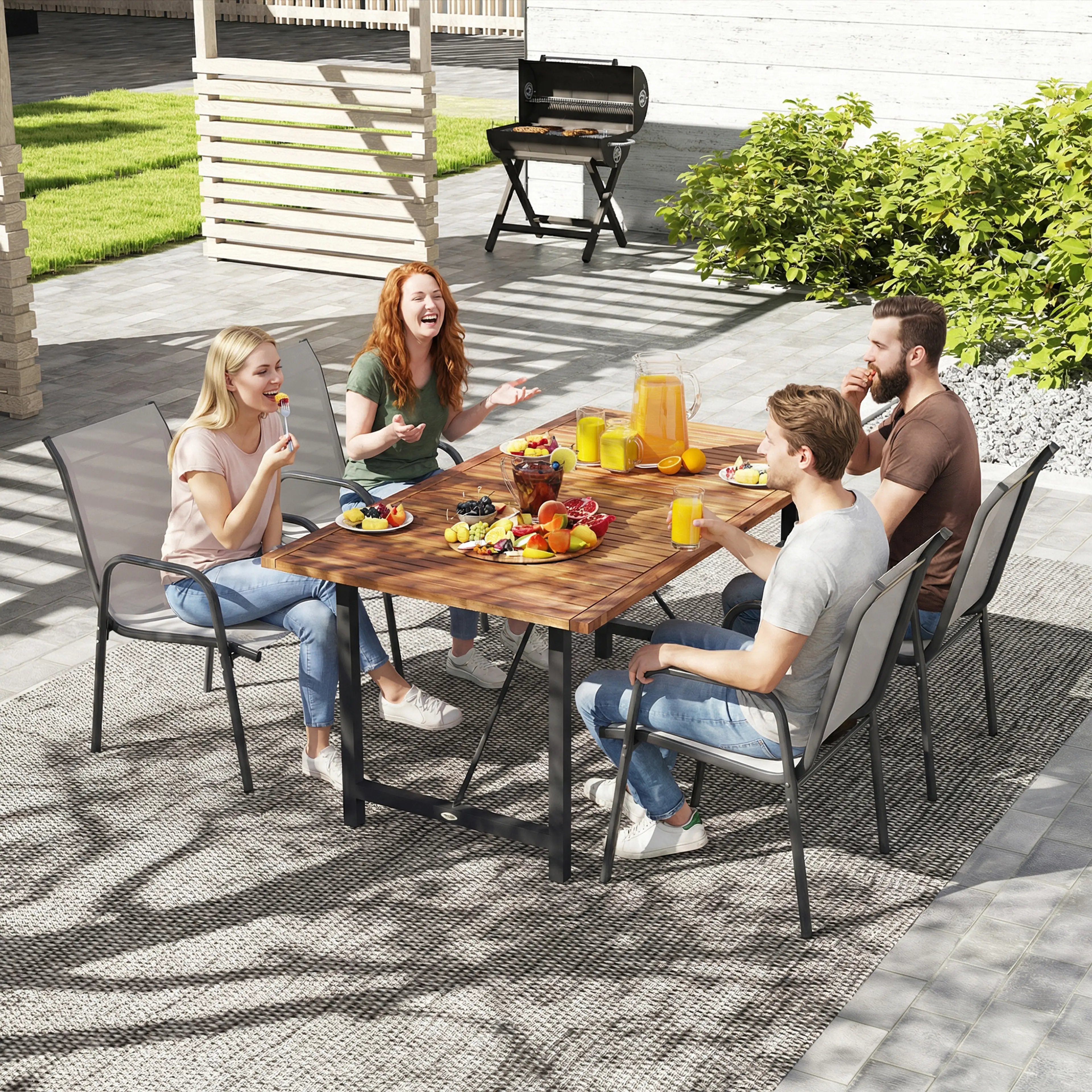 Fyra personer äter frukt och dricker saft vid ett långt träbord på en terrass, med en grill i bakgrunden