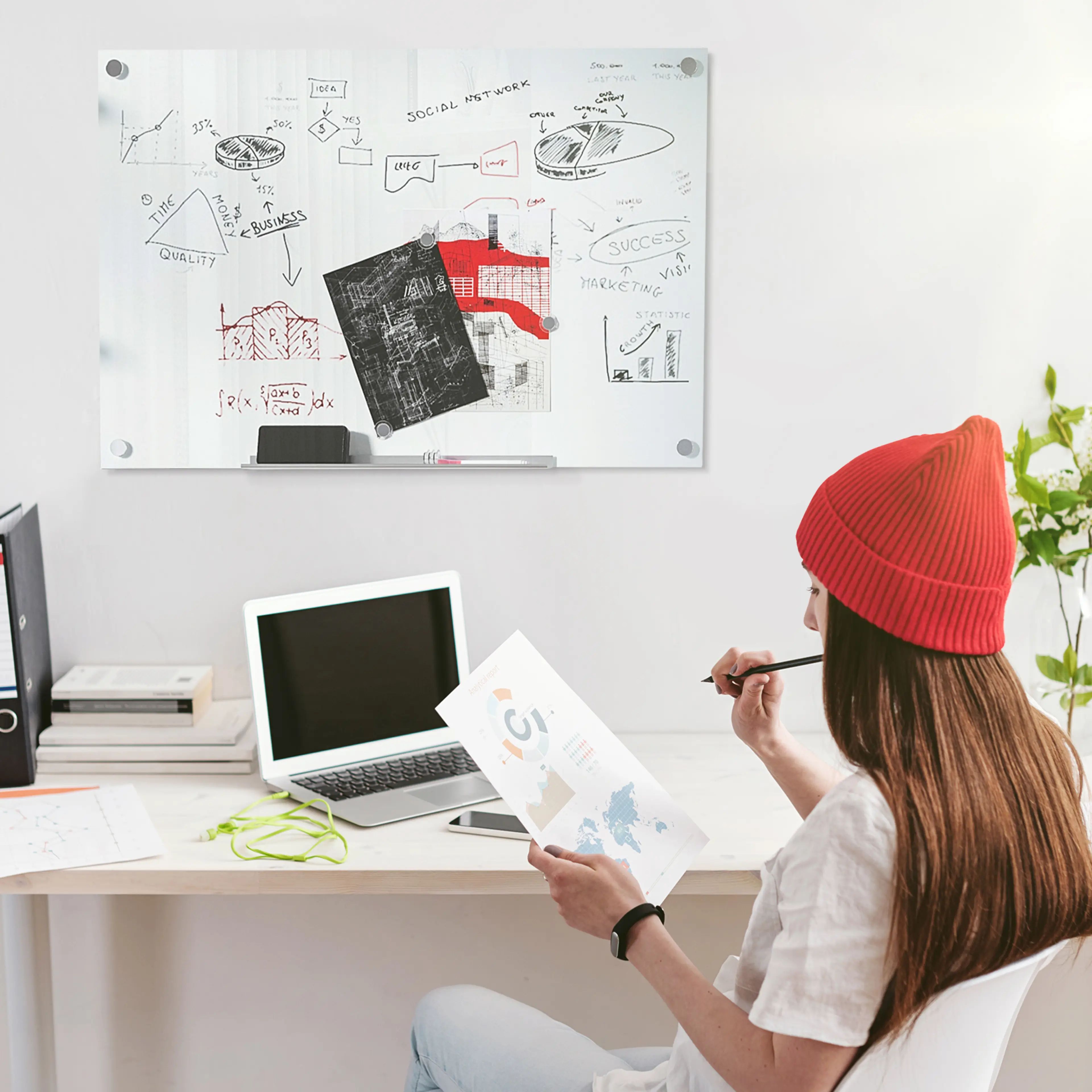 En kvinna vid ett skrivbord framför whiteboarden med anteckningar och papper