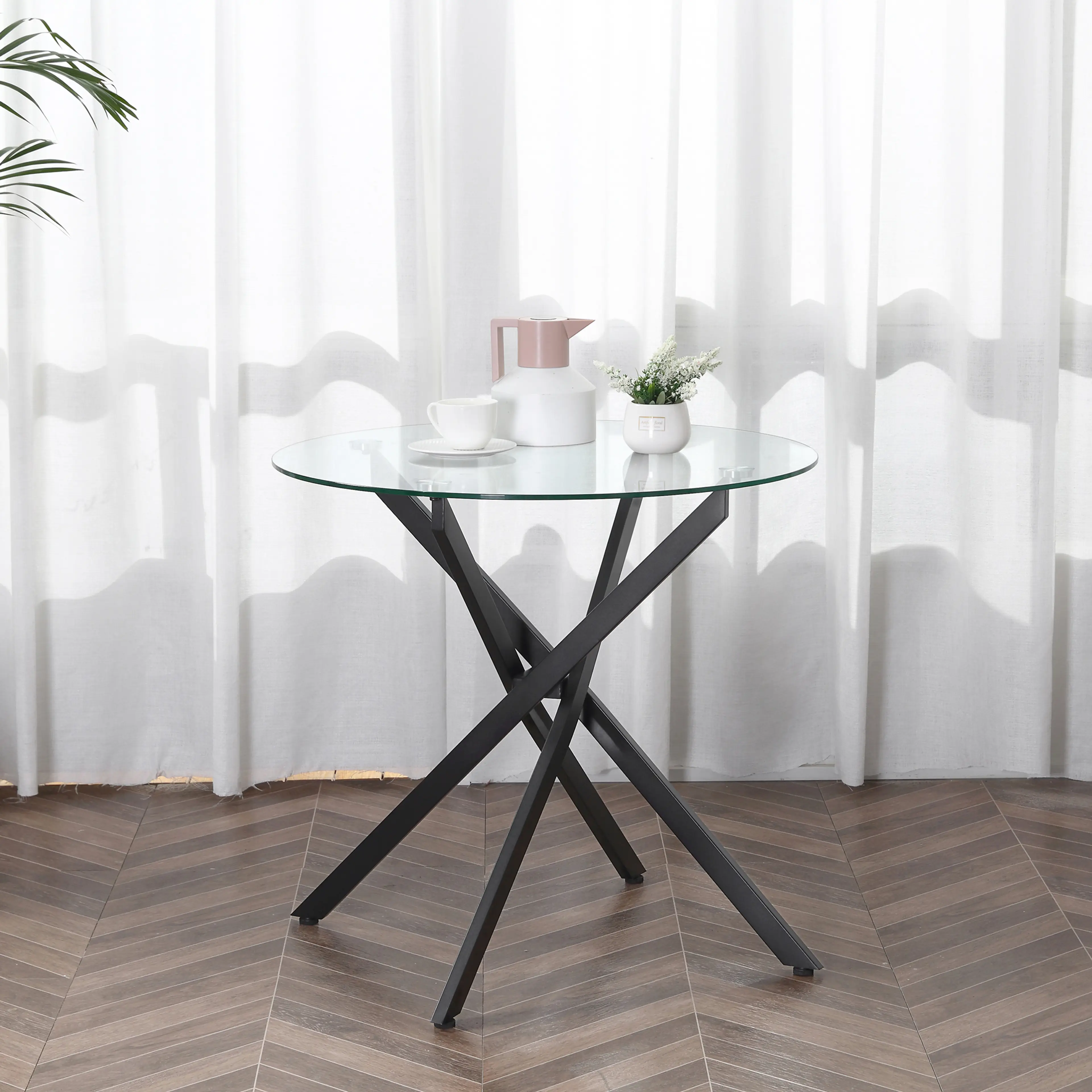 Glasbordet med en tekanna, en kopp och en krukväxt framför vita gardiner
