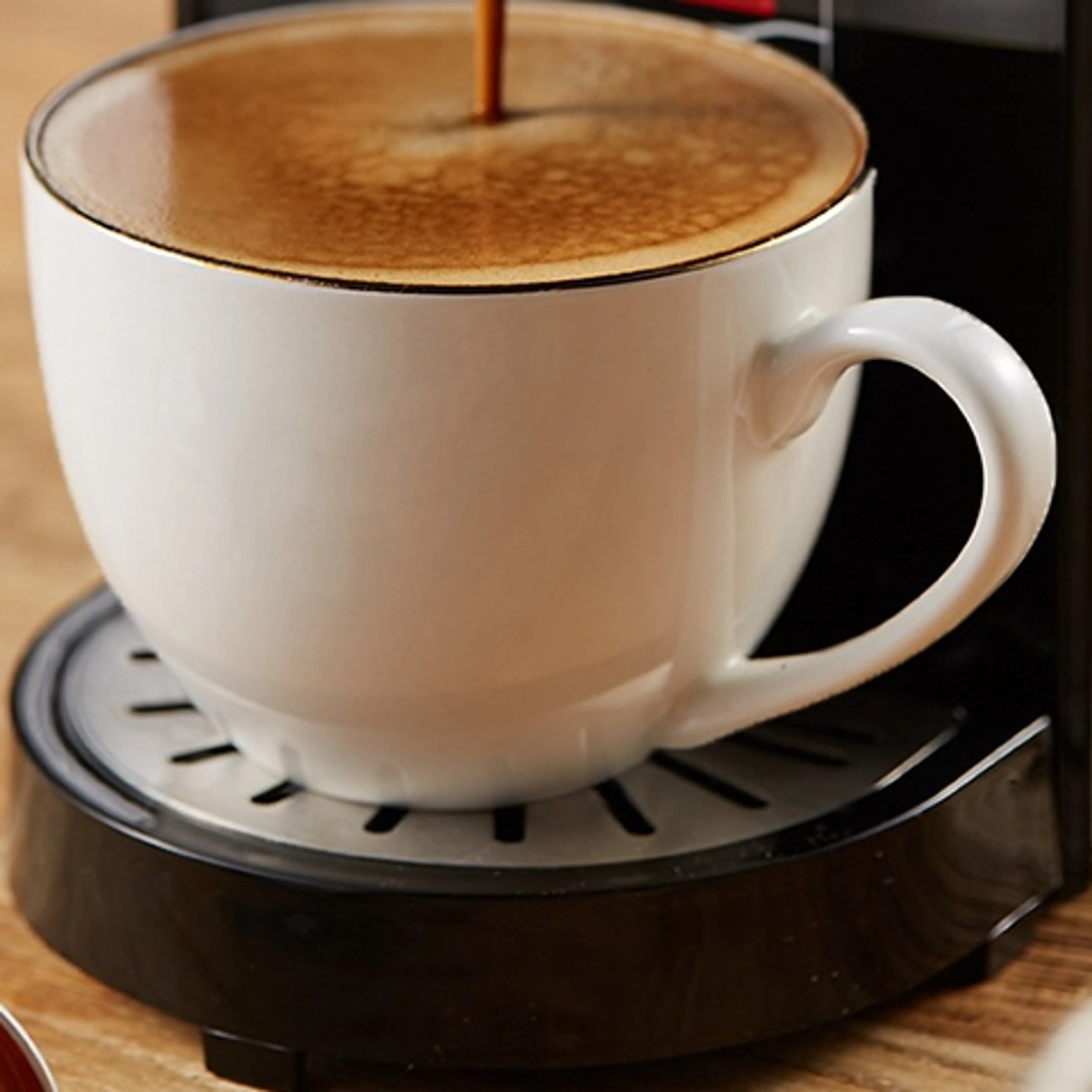 Kaffe rinner ner i en vit kopp med tjockt skum på maskinens droppgaller