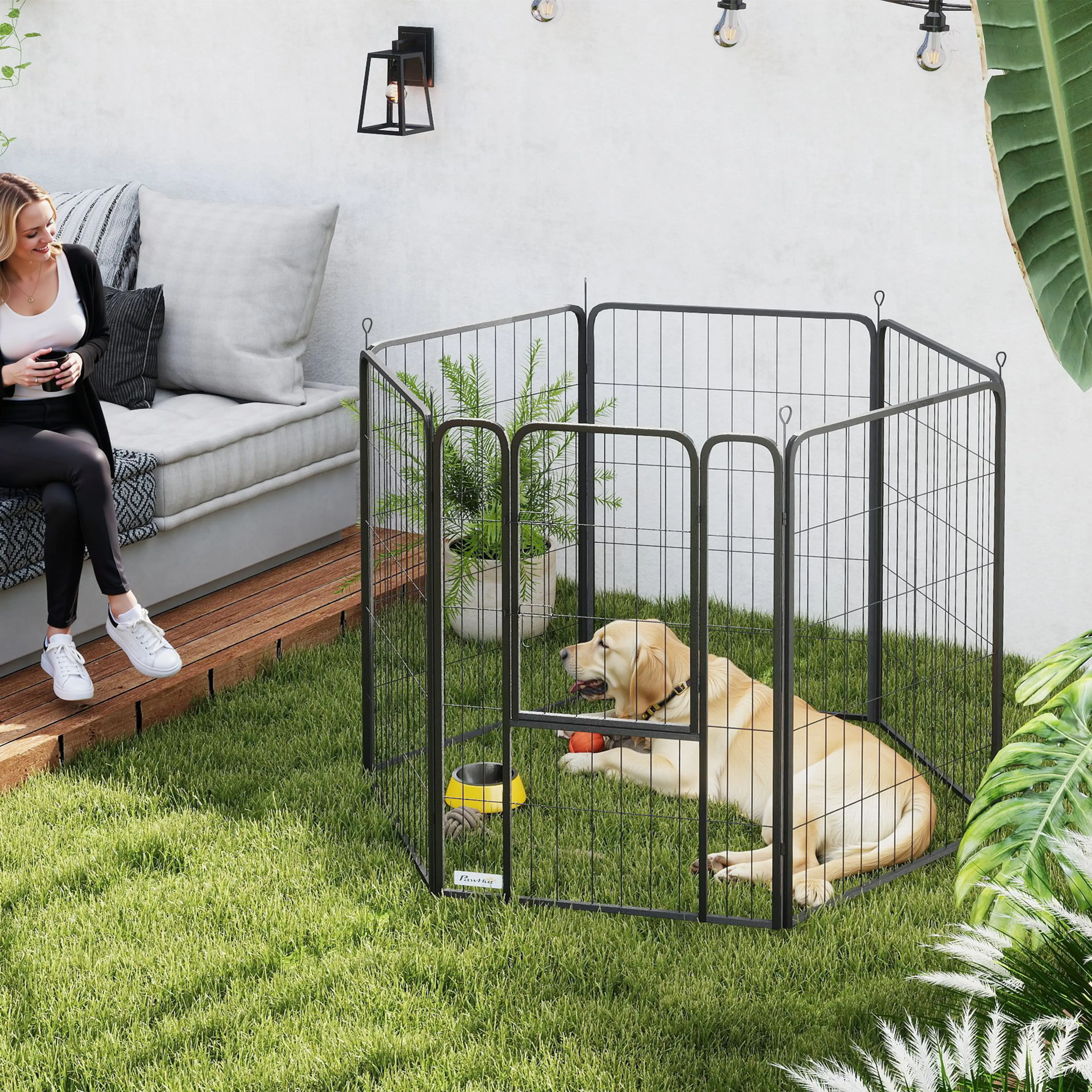 Hagen på en gräsmatta med en labrador inne, en gul skål och en röd boll, och en kvinna som sitter på en bänk bredvid