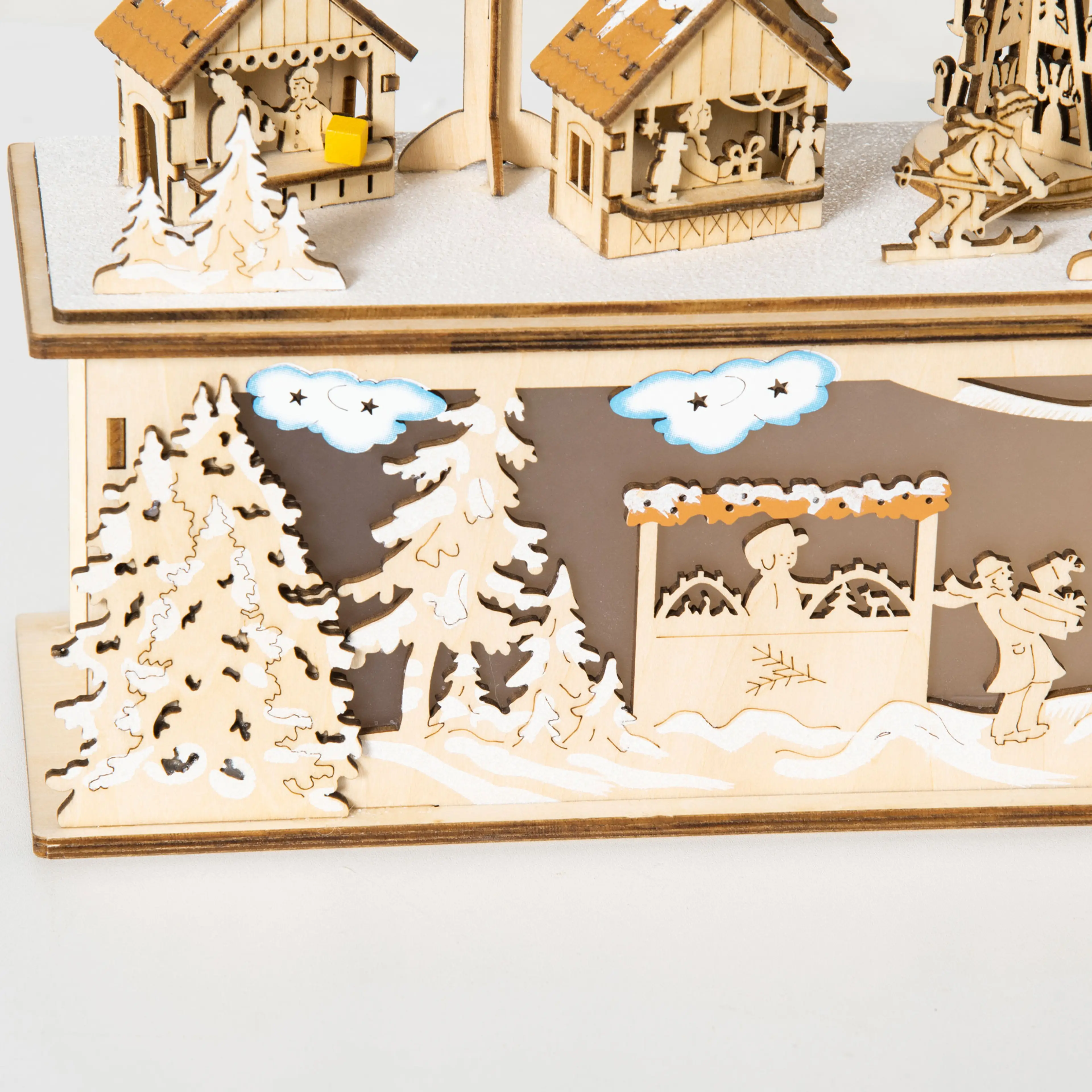 Närbild på julbyns framsida med utsågade granar, moln och figurer