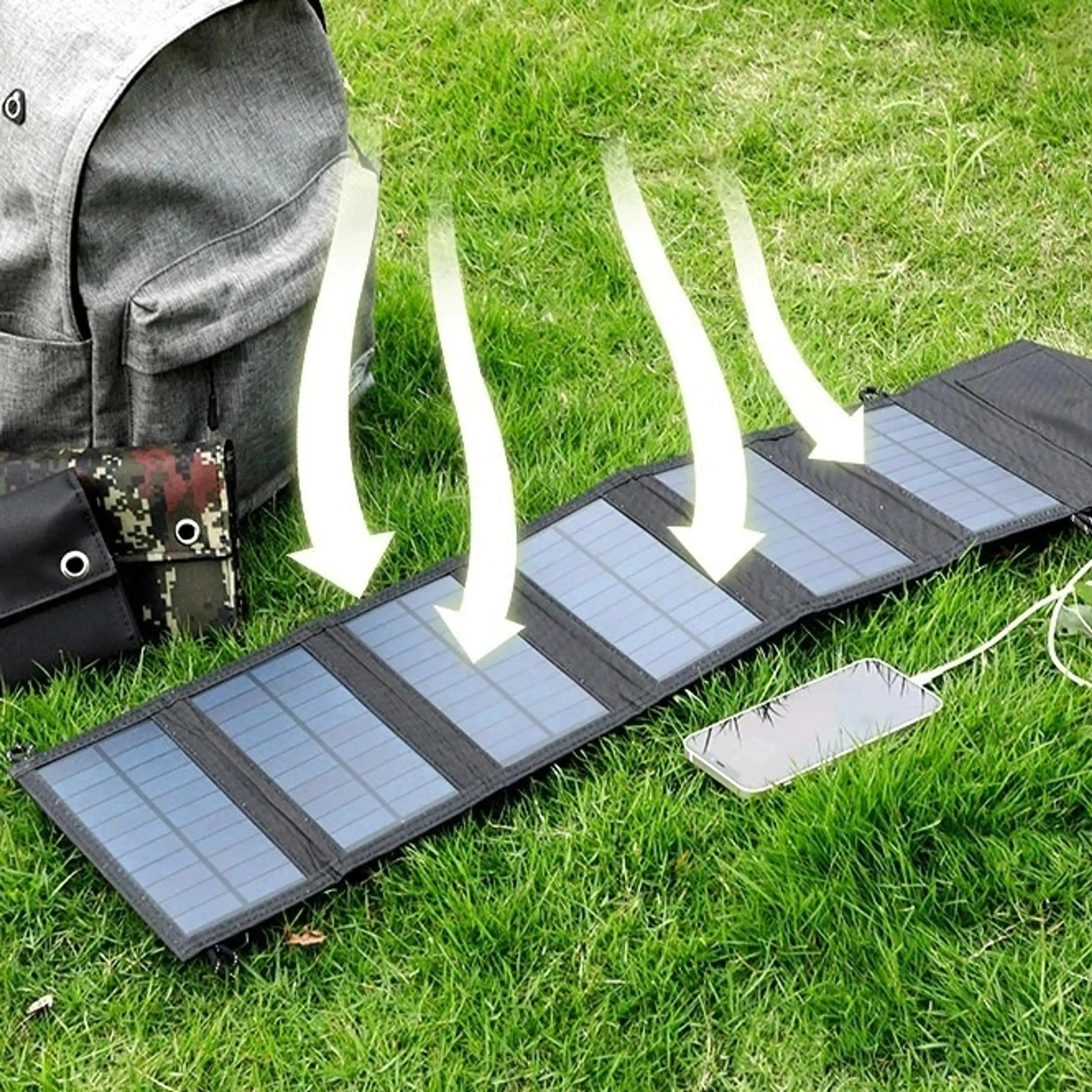Solpanelen utvikt i gräset bredvid ryggsäck och mobil som laddas