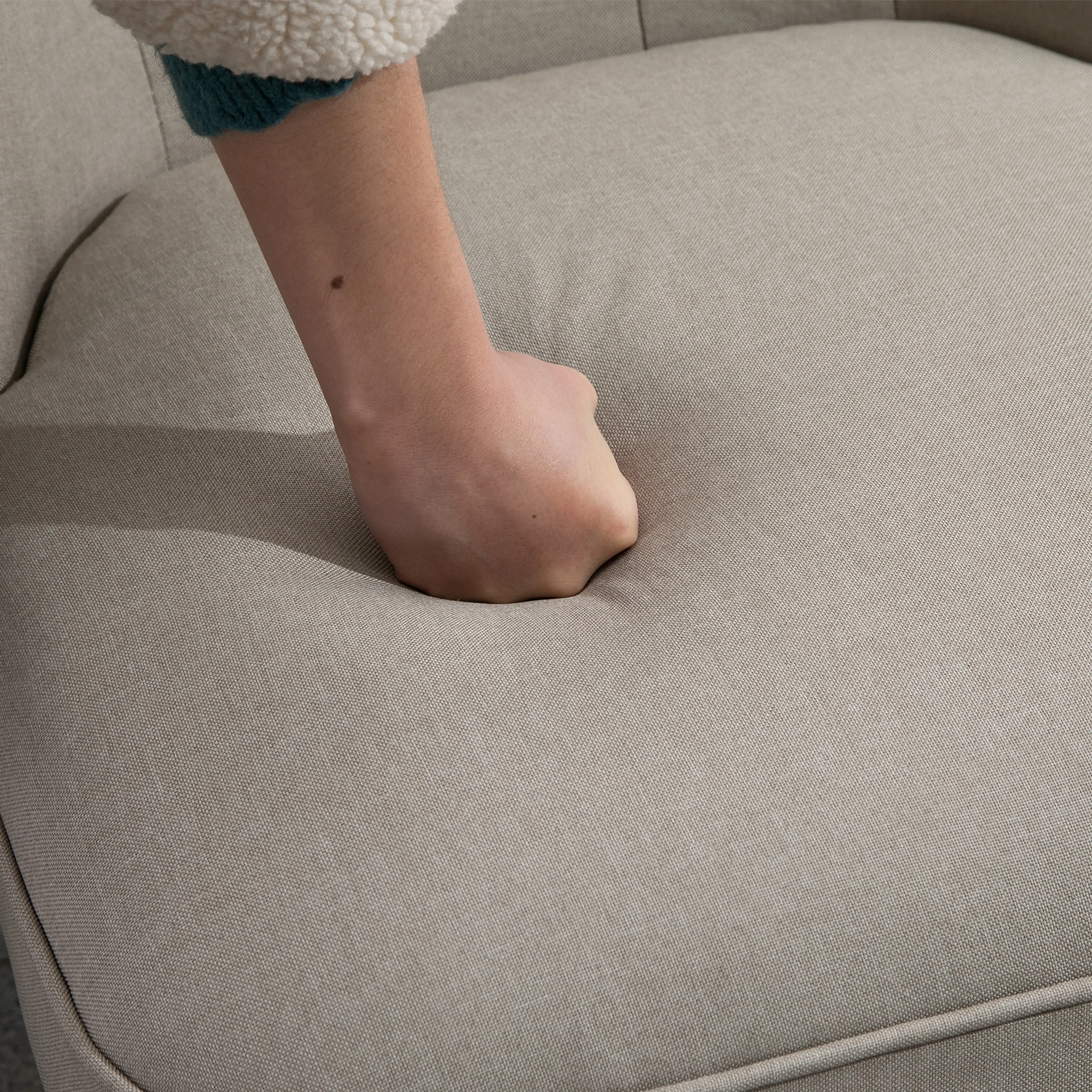Liten fåtölj i beige linne, en hand trycker ned sitsens stoppning
