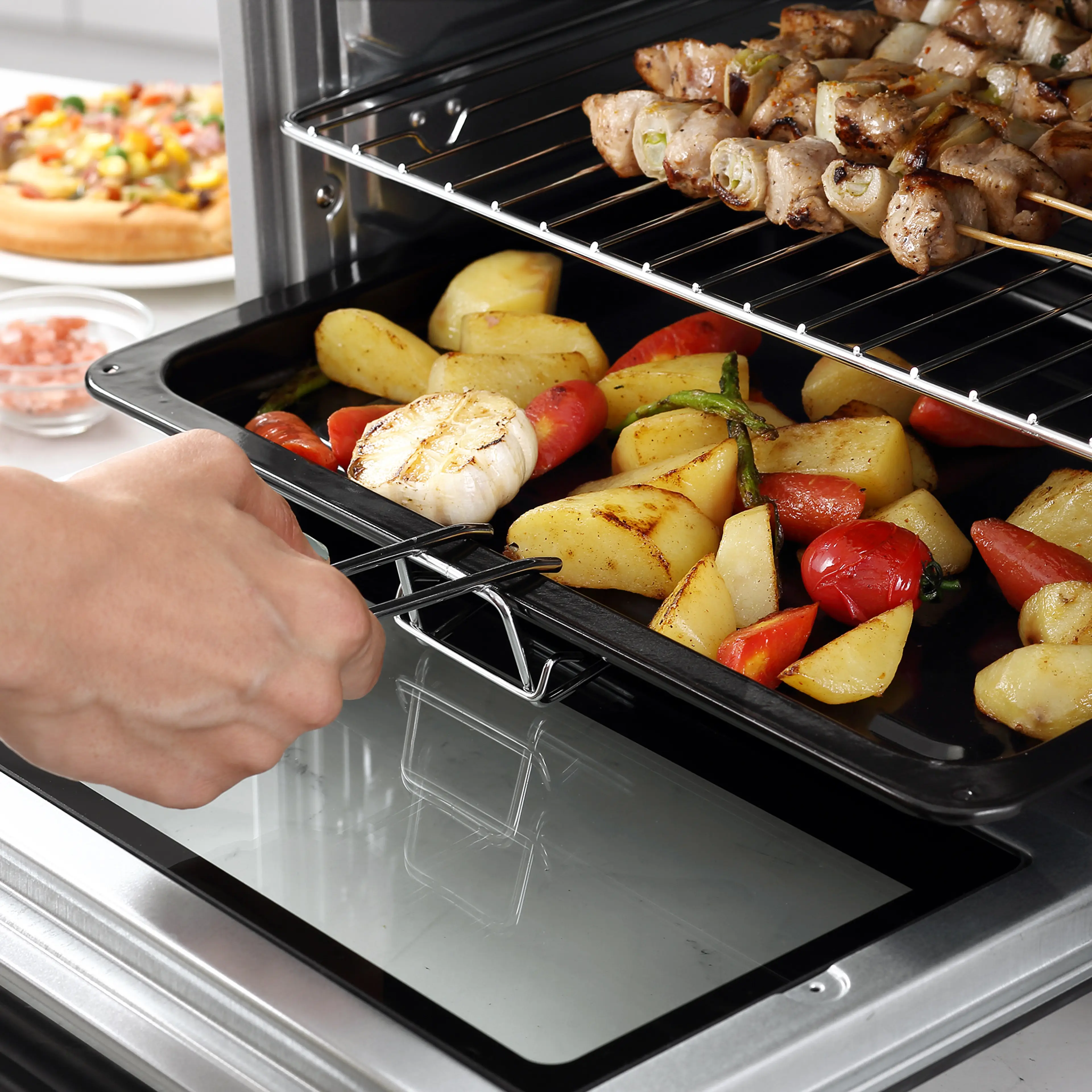 Grillspett och rotfrukter på gallret inne i den öppna miniugnen.