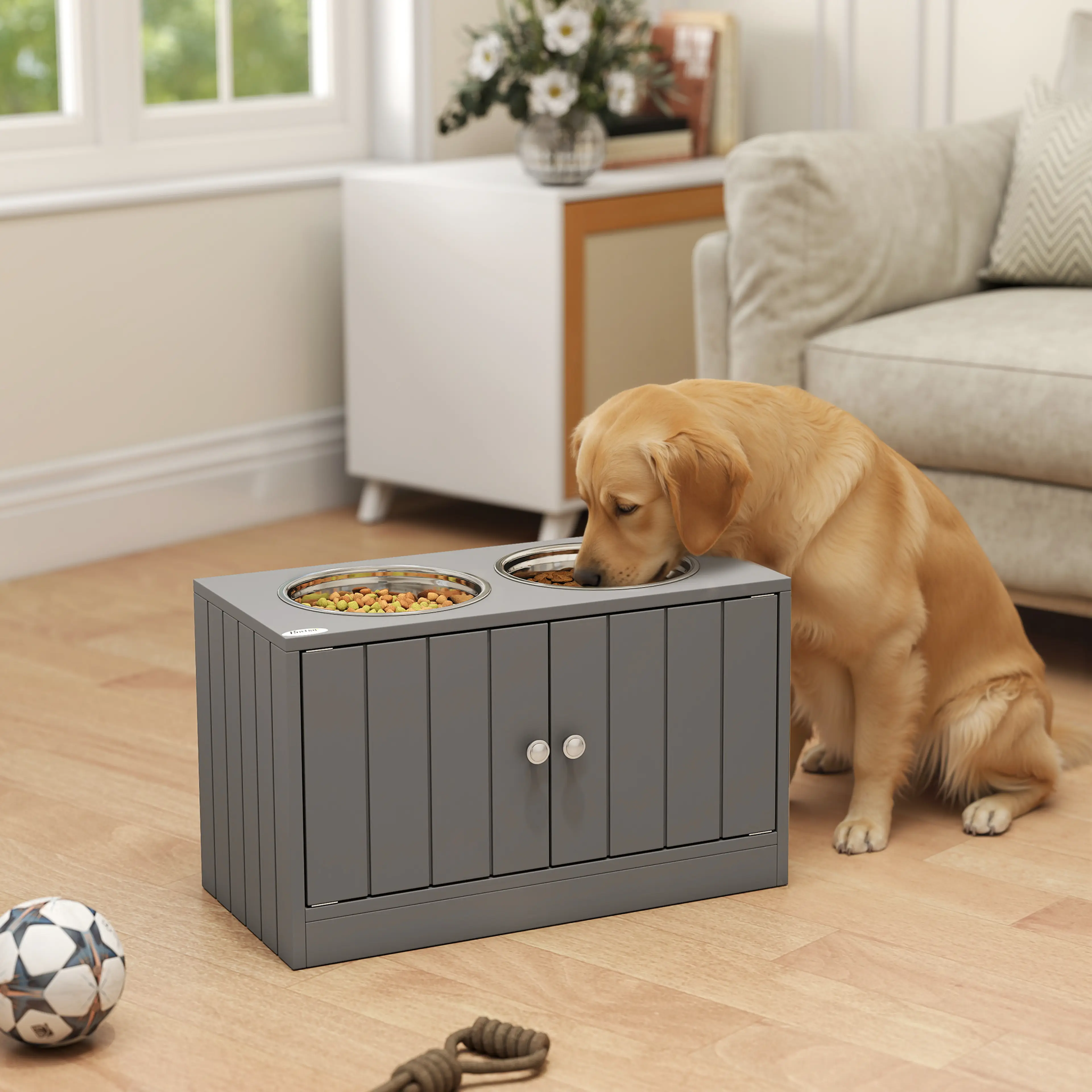 Golden retriever äter ur det gråa matskåpet framför en soffa