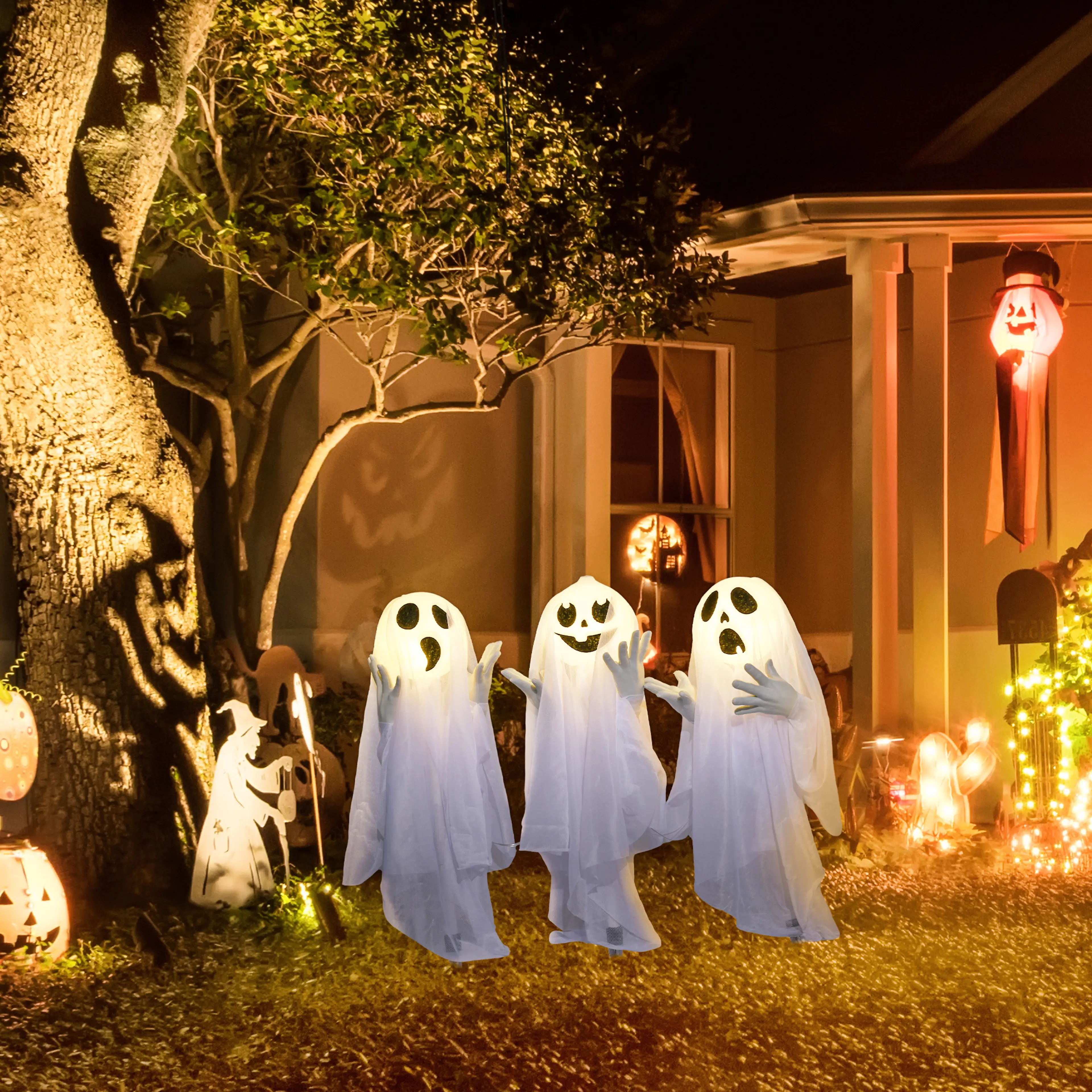 Spökena i en trädgård en halloweenkväll framför ett upplyst hus