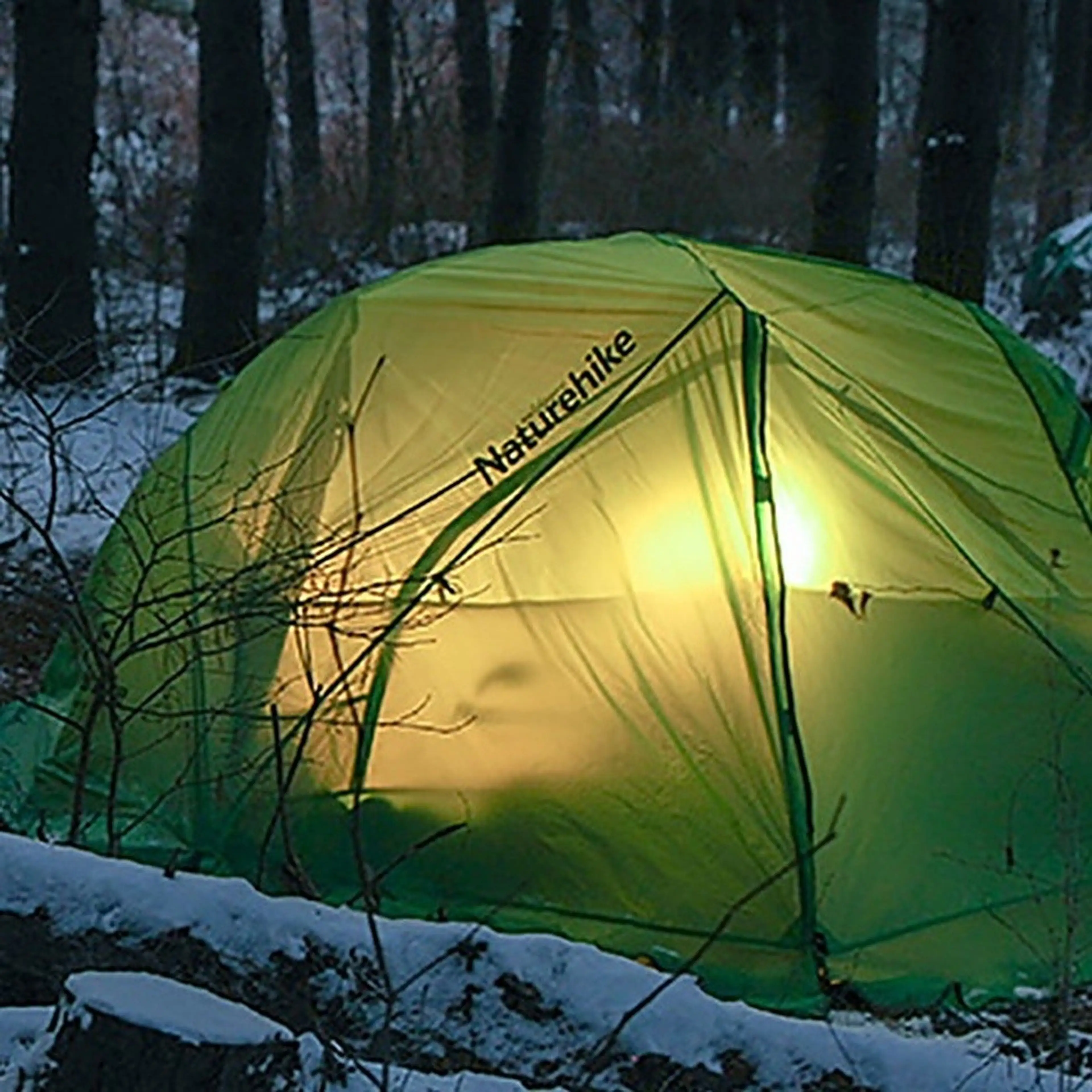 Campingtältet inifrån upplyst i en snötäckt skog i skymningen