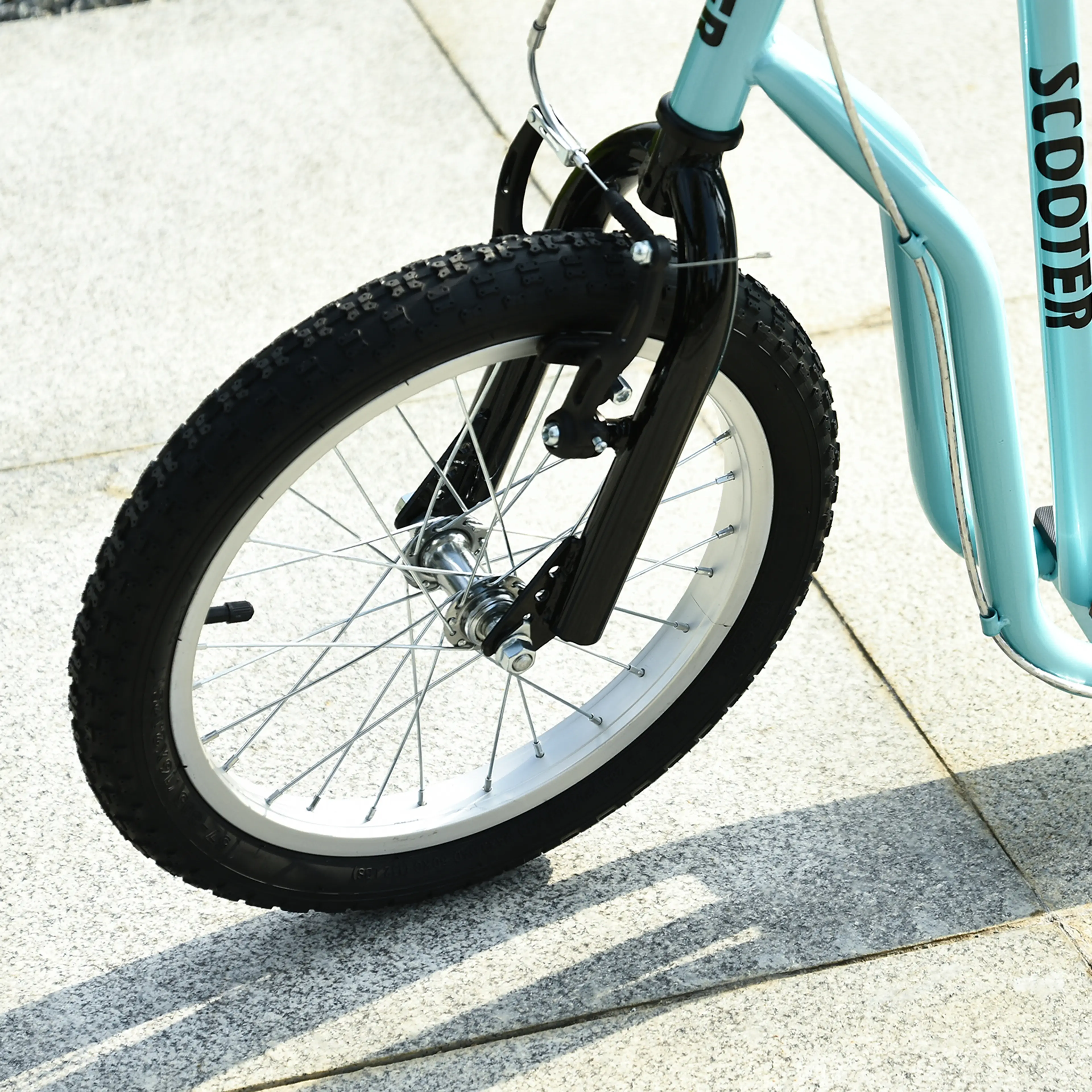 Närbild på det stora framhjulets däck och ekerfälg på turkos sparkcykel