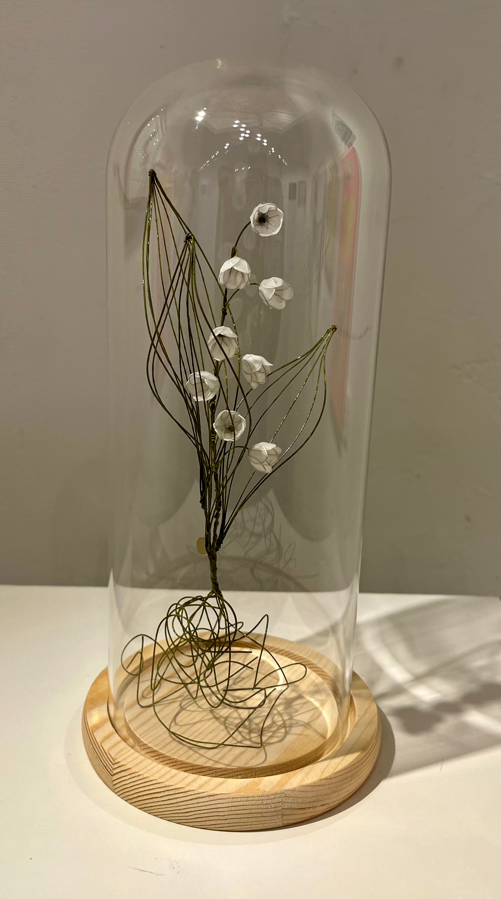 ガラスケースに入ったスズランのワイヤーアート作品。白い花と緑色の葉が美しい。 410 Web Store。