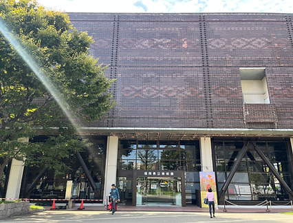 Entrance to the Fukuoka Prefectural Museum of Art, brick wall and trees. Two people are walking. Spatial Art TORAM
