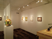 アートギャラリーの白い壁に絵画が展示され、金色の彫刻がある室内。