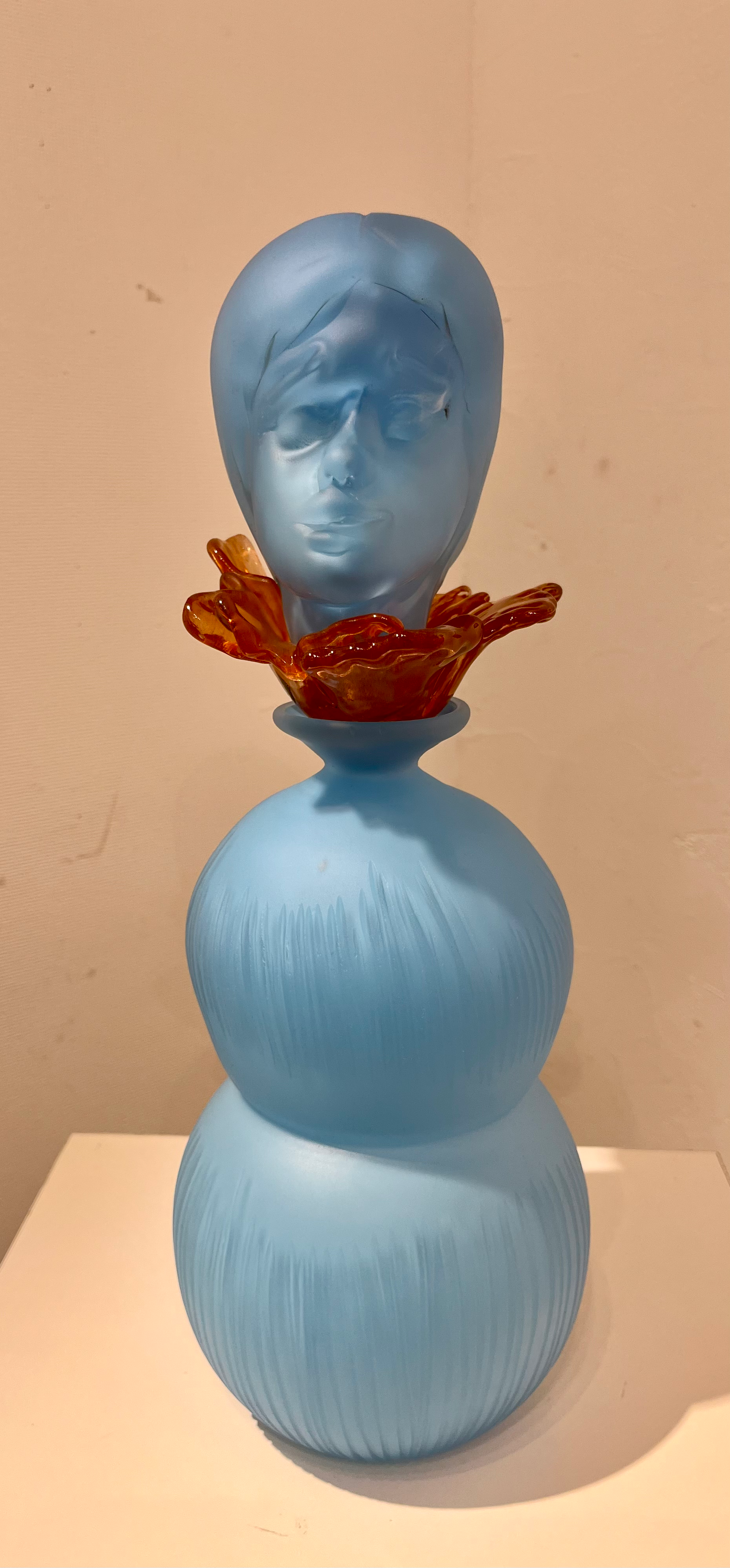 青い彫刻の像、顔とオレンジ色の花。 イワイヨシコが作った芸術作品のクローズアップ。