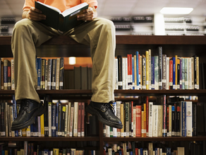 Pessoa sentada sobre estante de biblioteca lendo livro.