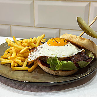 Loaded Aussie-style beef burger with fried egg, bacon, lettuce and pickled gherkin on brioche bun served with golden crispy fries on a dark plate, casual catering menu option at Château Destinée private event venue in Dordogne France