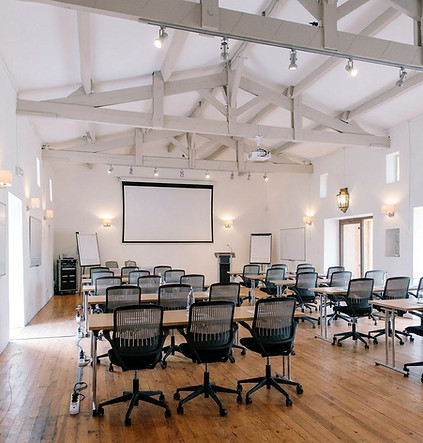 Historic event barn at Château Destinée arranged classroom-style for a corporate seminar, with exposed white beams, projector screen, presentation podium and flexible meeting tables