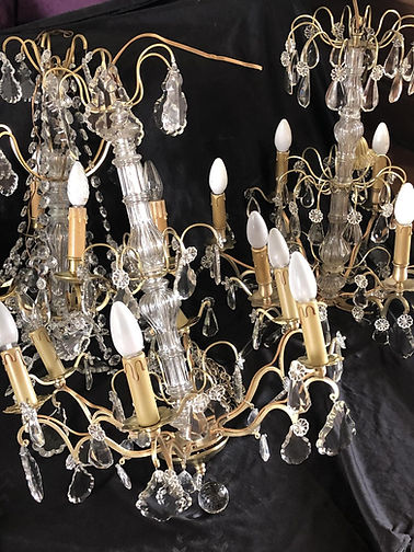 Pair of grand Maria Theresa-style crystal chandeliers with gilt brass frames, crystal rosettes, and cascading beaded chains displayed against dark fabric backdrop at Château Destinée