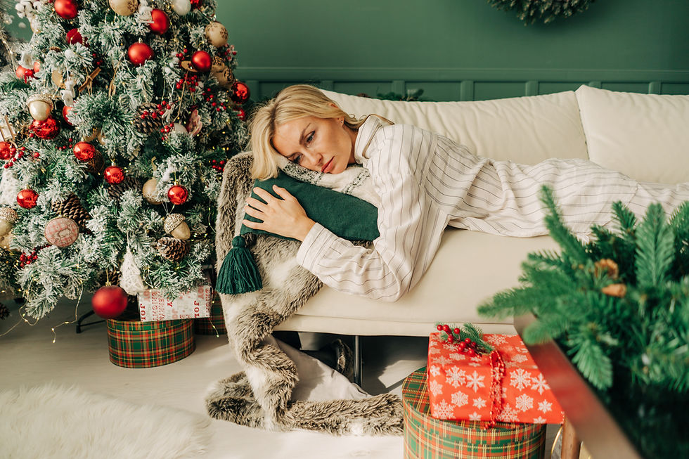 Woman in pajamas rests on a couch, holding a green pillow. A decorated Christmas tree and gifts with red and plaid patterns are behind her.