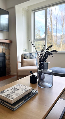 Whistler condo living room with coffee table styling, lounge chair, fireplace, large window, and mountain view.