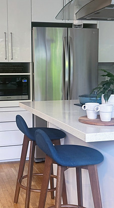 North Vancouver condo kitchen with white cabinetry, stainless steel appliances, blue island stools, wood flooring, and open residential layout.