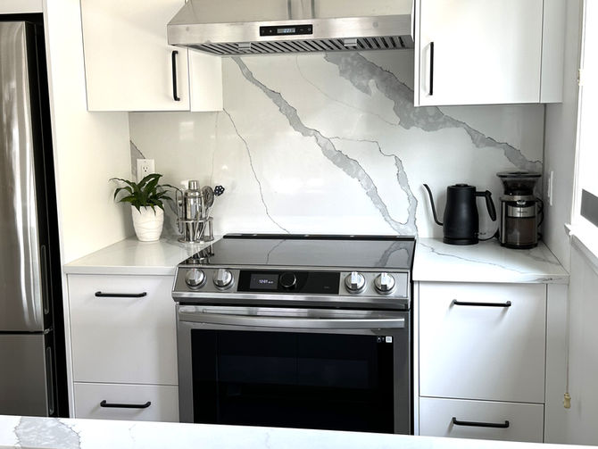 Renovated kitchen with stainless steel range, white cabinetry, black hardware, and marble-look backsplash detail.