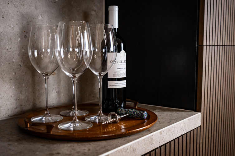 Close-up of wine bottle, glassware, and tray styled within a custom stone and wood bar niche.