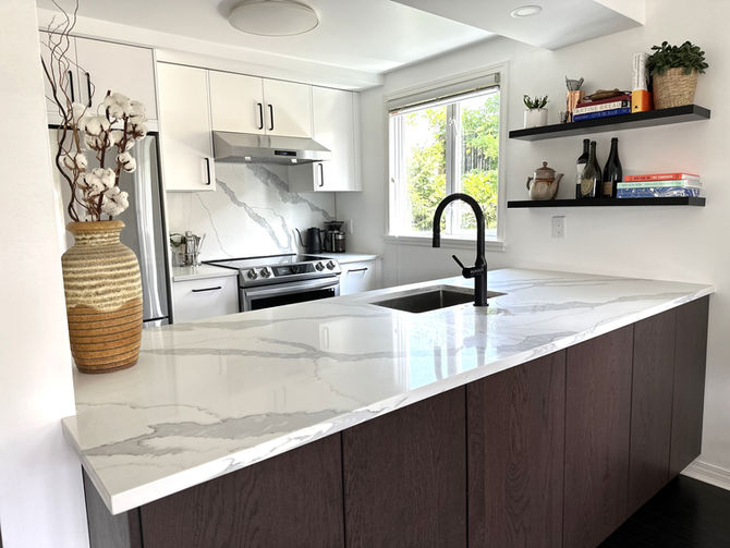 Renovated galley kitchen with white upper cabinets, dark lower cabinetry, marble-look counters, black faucet, and natural light.