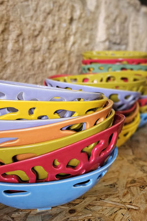 Vista lateral de cuencos calados apilados en lila, amarillo, naranja, verde oliva, rojo y azul sobre una repisa de madera