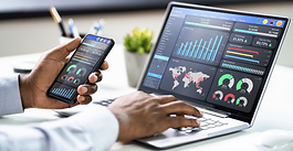 User reviewing analytics dashboards on a laptop and smartphone at a desk.