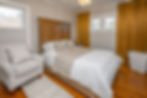 Bedroom featuring a wooden bed, striped armchair, and white rug