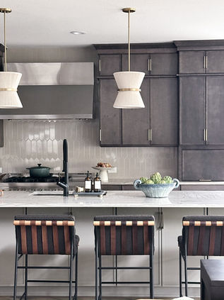 Kitchen island with dark cabinetry, marble-look countertop, black faucet, pendant lights, leather bar stools, and textured backsplash tile.
