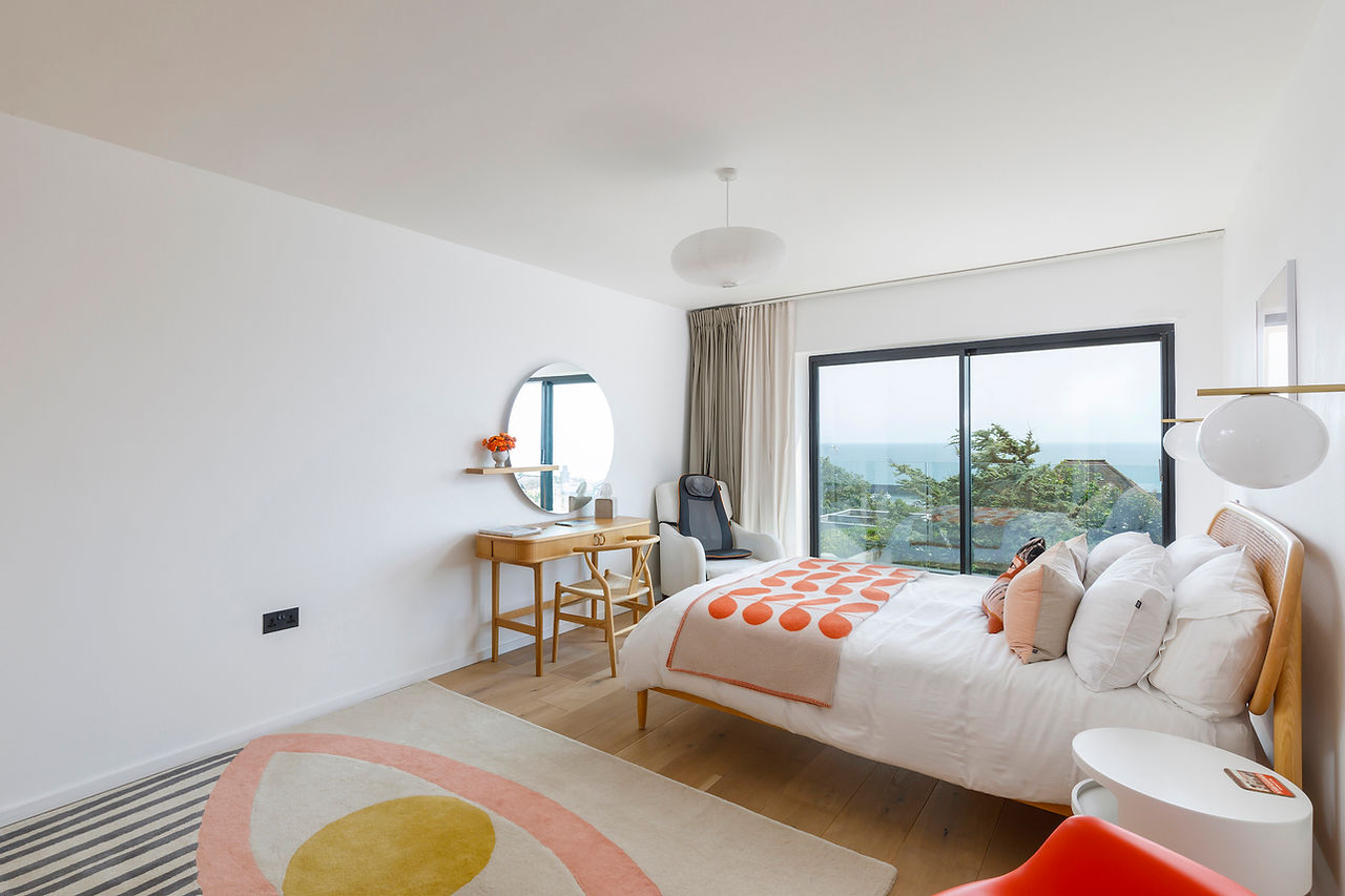Modern bedroom with sliding doors opening to sea views, wood flooring, and dresser and chair