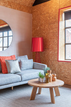 Detail view of living area featuring grey sofa, round wooden coffee table and red floor lamp against textured wall