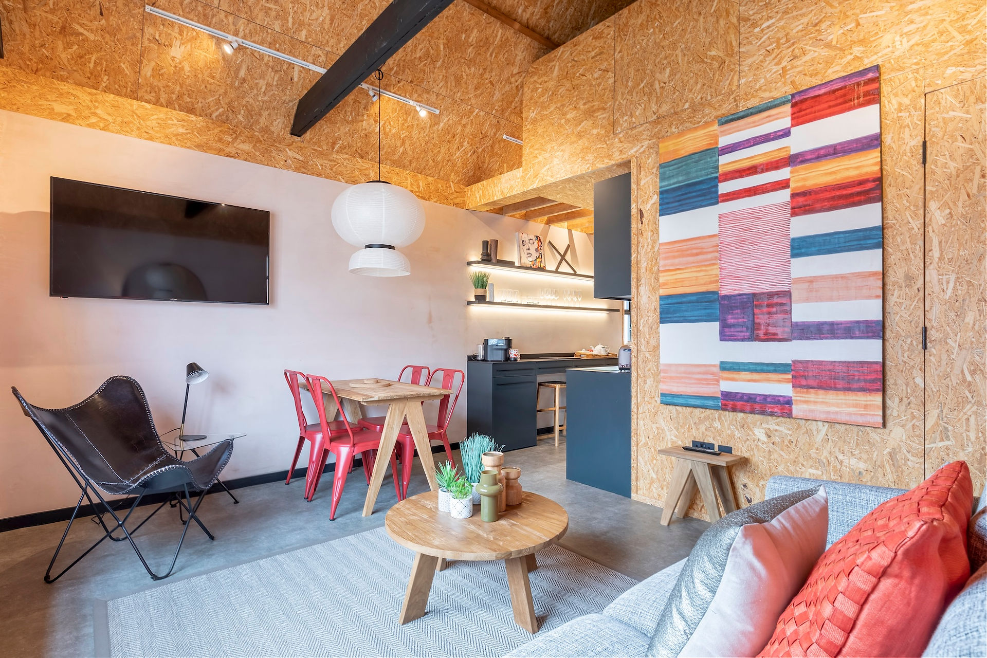 Open-plan living space with dining table, wall-mounted television and compact kitchen in a modern loft-style interior