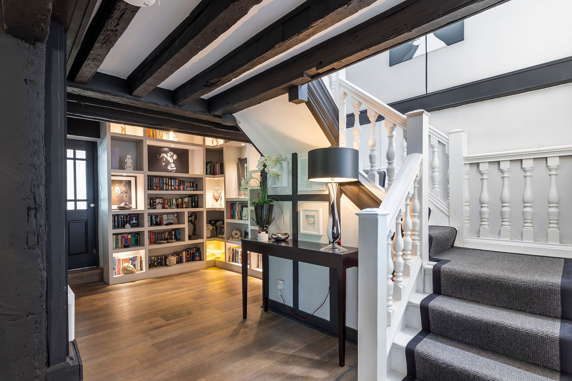 Hallway with exposed timber beams, built-in bookshelves, console table, and staircase with carpeted steps
