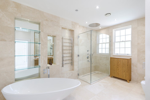 High-end bathroom with freestanding bathtub, marble tiles, glass walk-in shower and built-in shelving in luxury British home