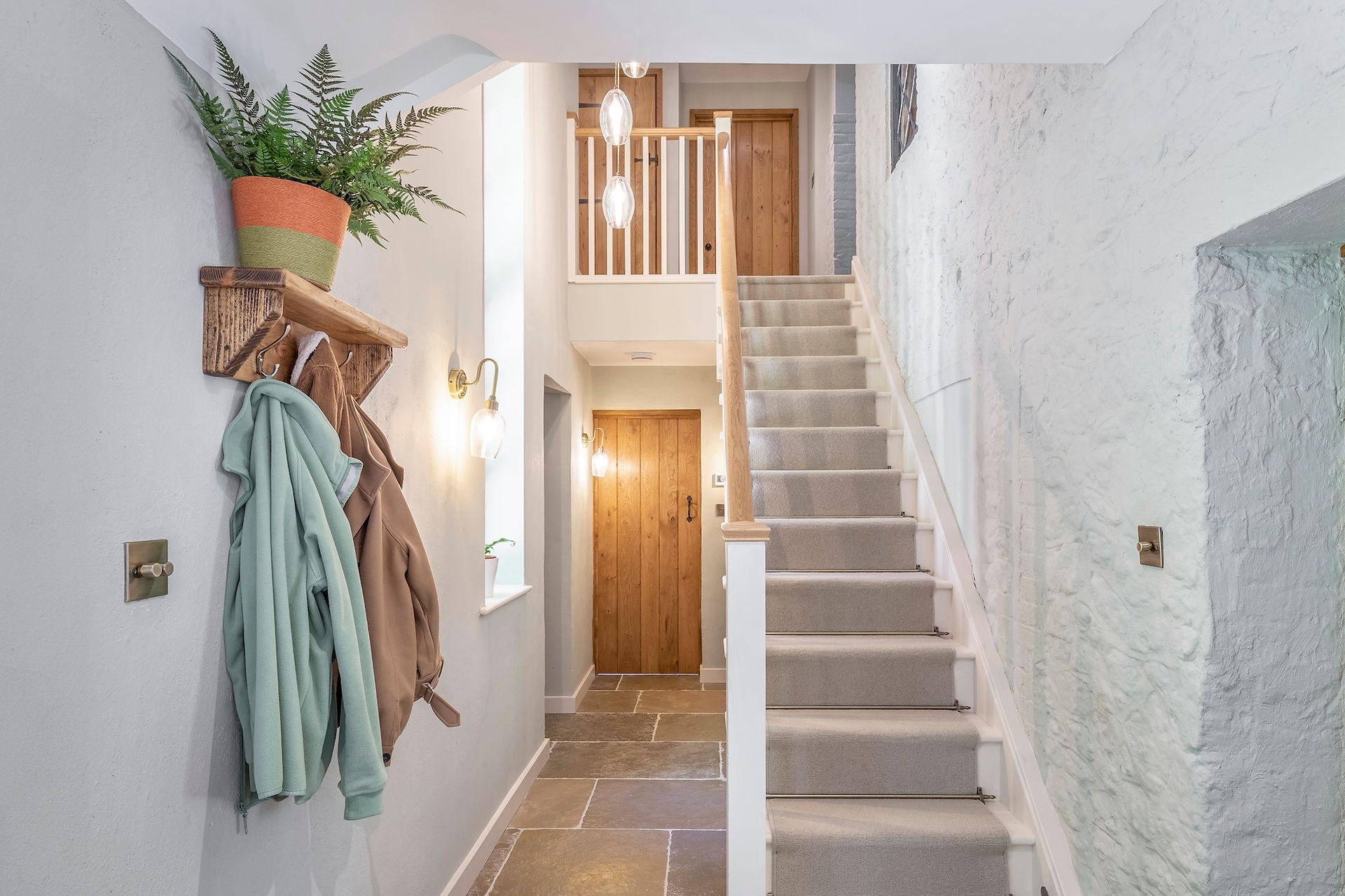 Modern rustic hallway with stone flooring, white staircase, natural wood doors, and coat hooks