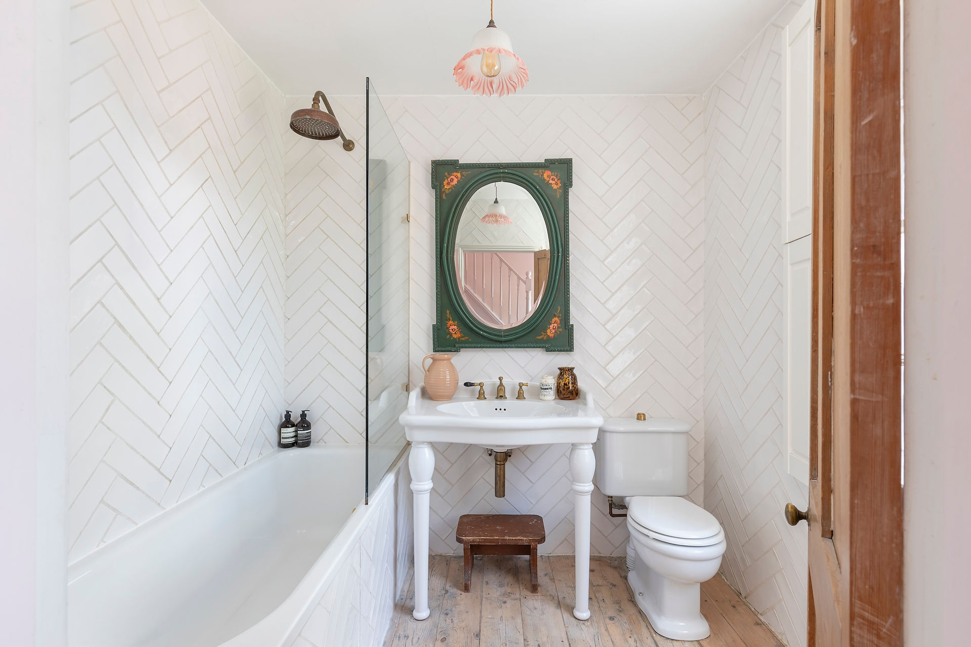 Bathroom with freestanding bath, herringbone tiled walls, pedestal sink, vintage mirror and pink accents