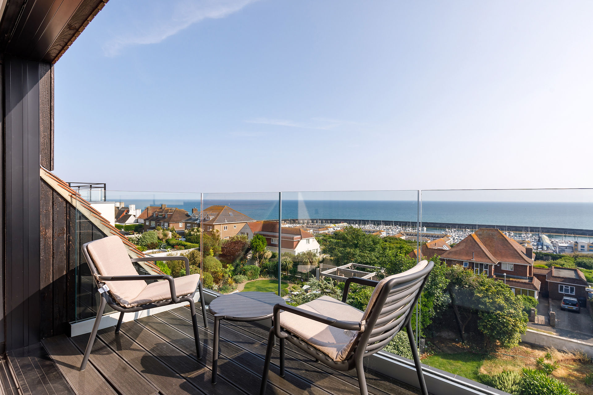Balcony with seating and glass balustrade, overlooking the sea and surrounding rooftops
