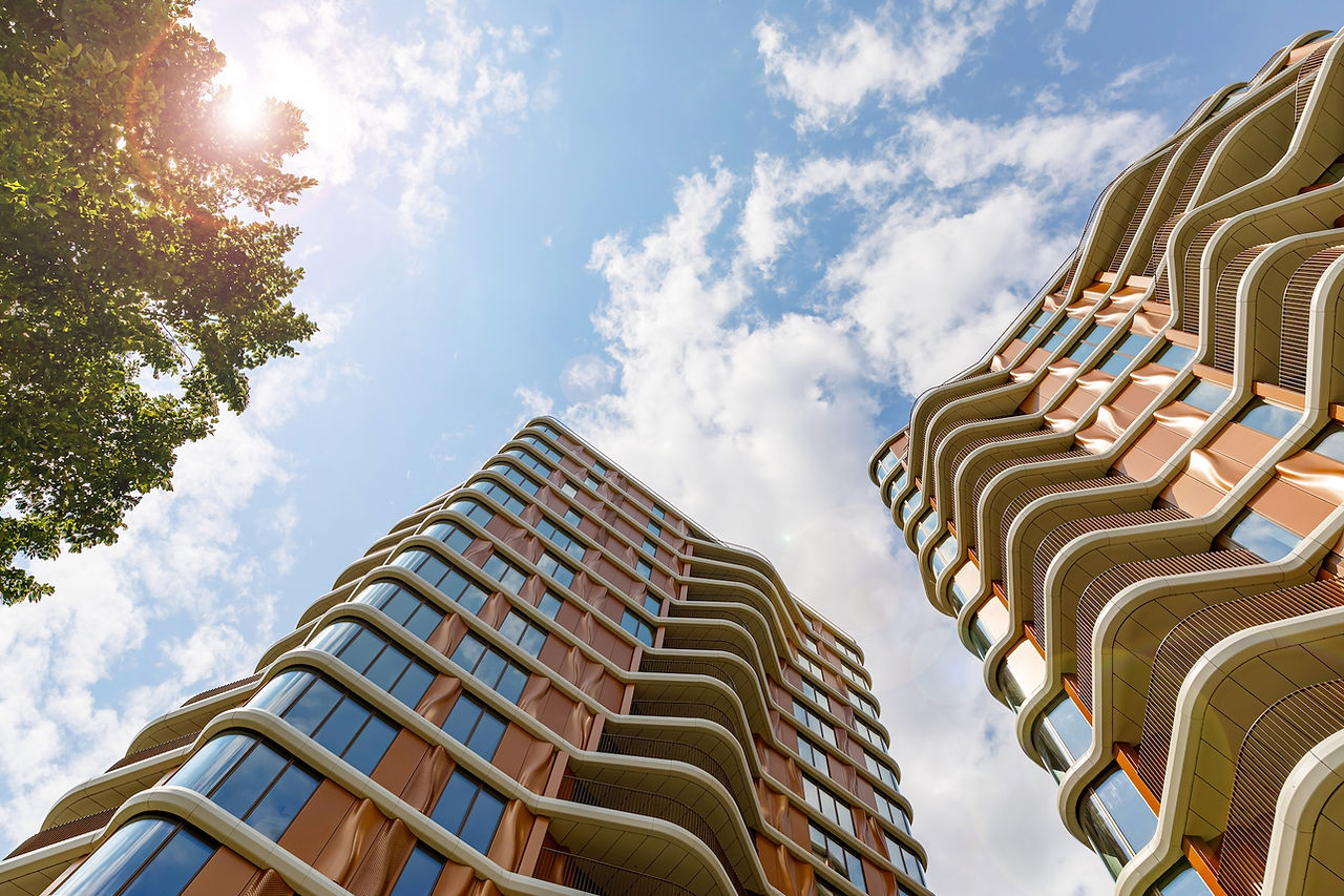 Low-angle view of Triptych Bankside in London. A contemporary building with curved balconies and copper-toned façade against a blue sky